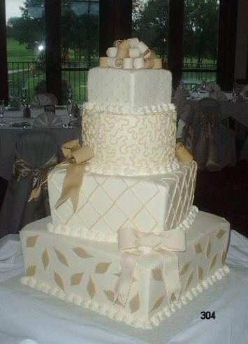 Four-tier white wedding cake with gold ribbon details and a topper on a decorated table