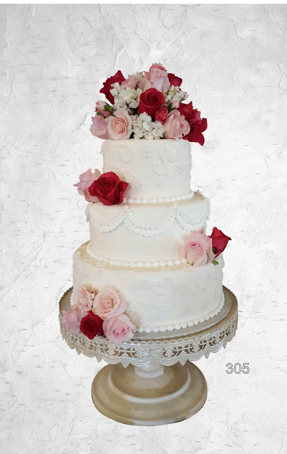 Three-tier white wedding cake with pink and red flowers on a gold stand