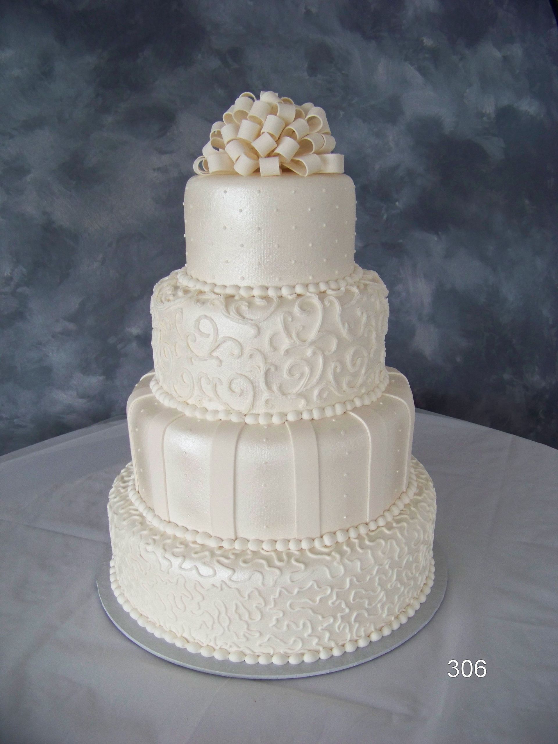 Four-tier white wedding cake with ornate frosting and a cluster of flowers on top