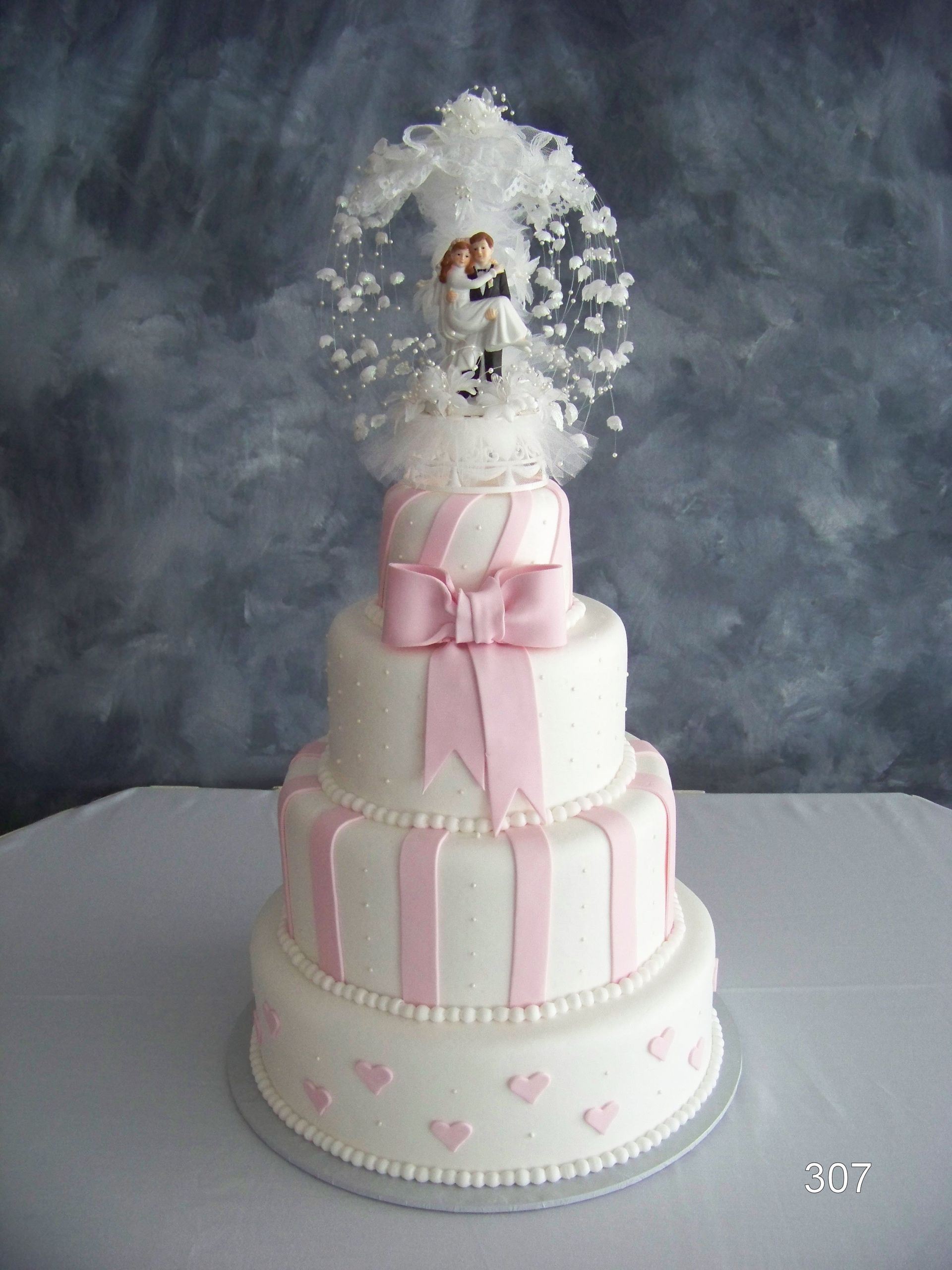 Three-tier pink and white cake with a small dog topper and white floral decorations on a gray backdrop