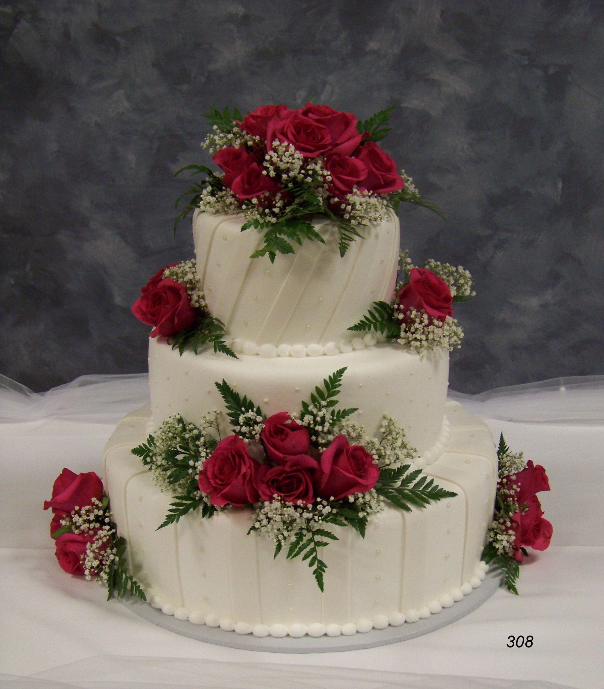 Three-tier white wedding cake with red rose decorations on a gray backdrop