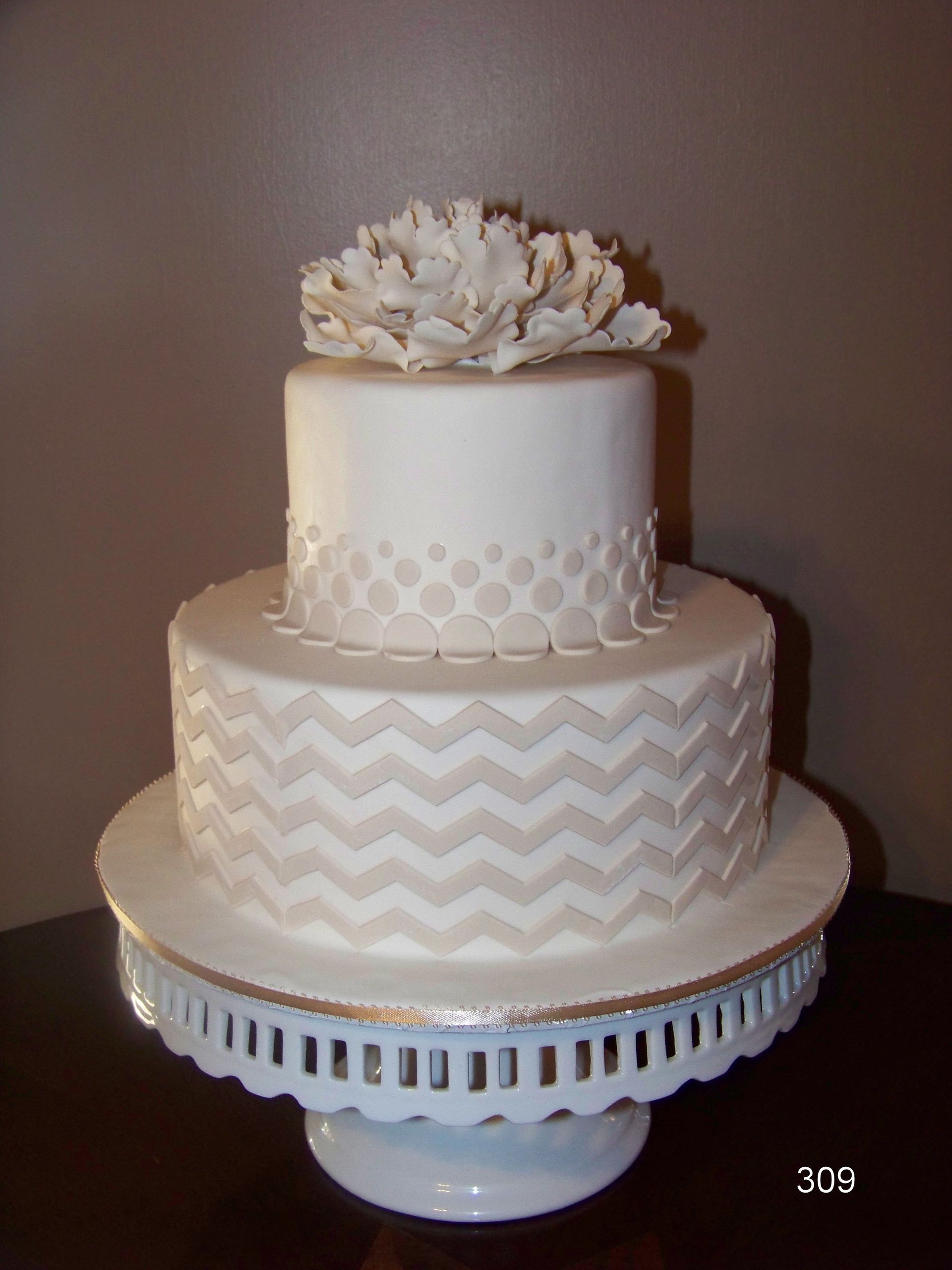 Three-tier white wedding cake with decorative patterns and floral topper on a pedestal stand