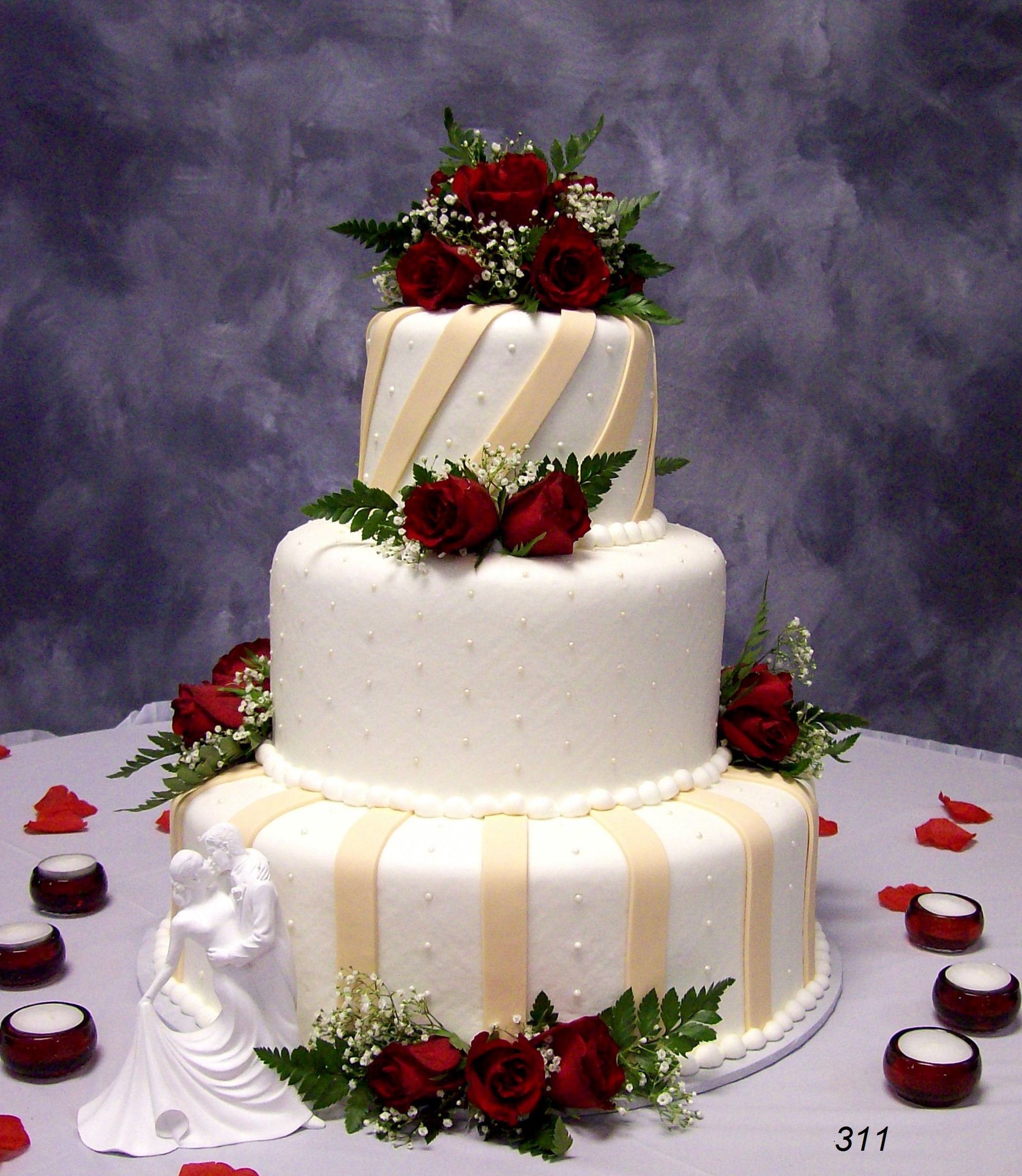 Three-tier white wedding cake with red roses and cream ribbons on a gray backdrop