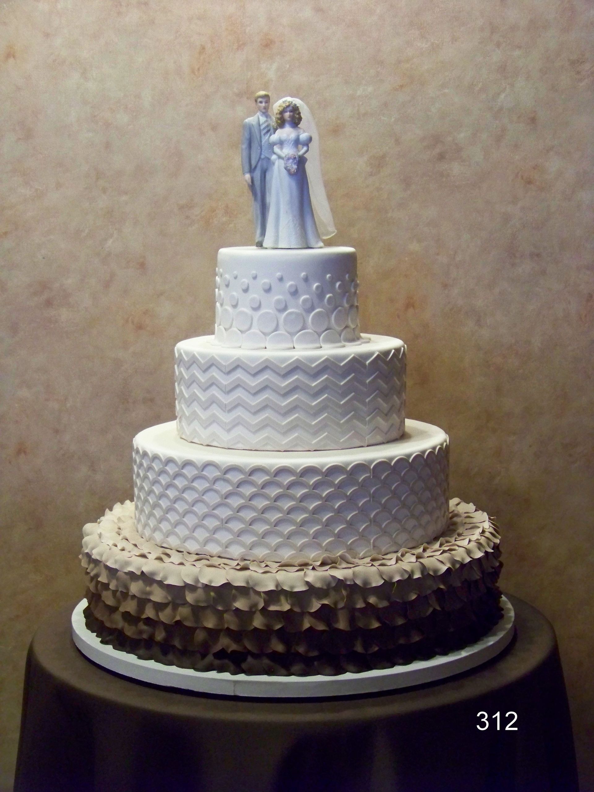 Tiered wedding cake with white textured layers and a bride-and-groom topper