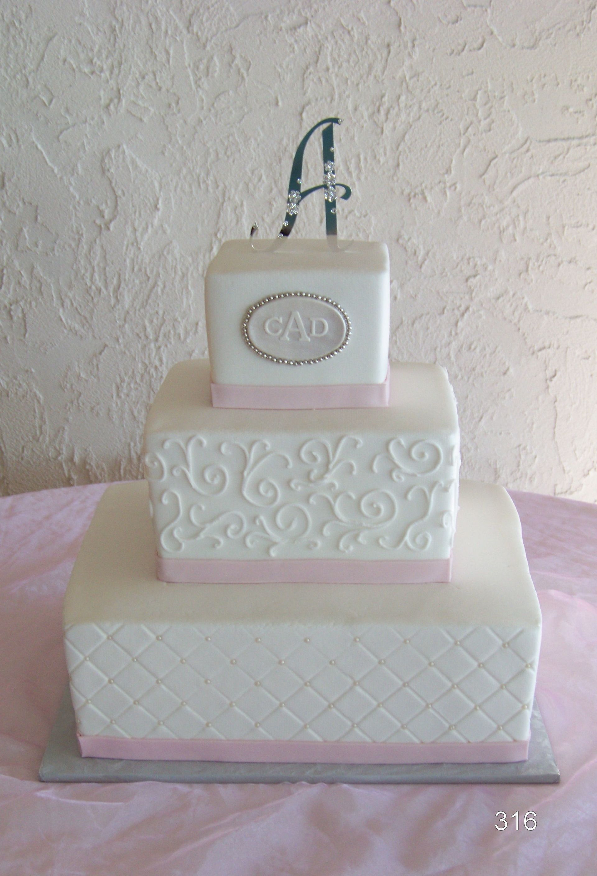 Three-tier white wedding cake with pink accents and decorative silver topper