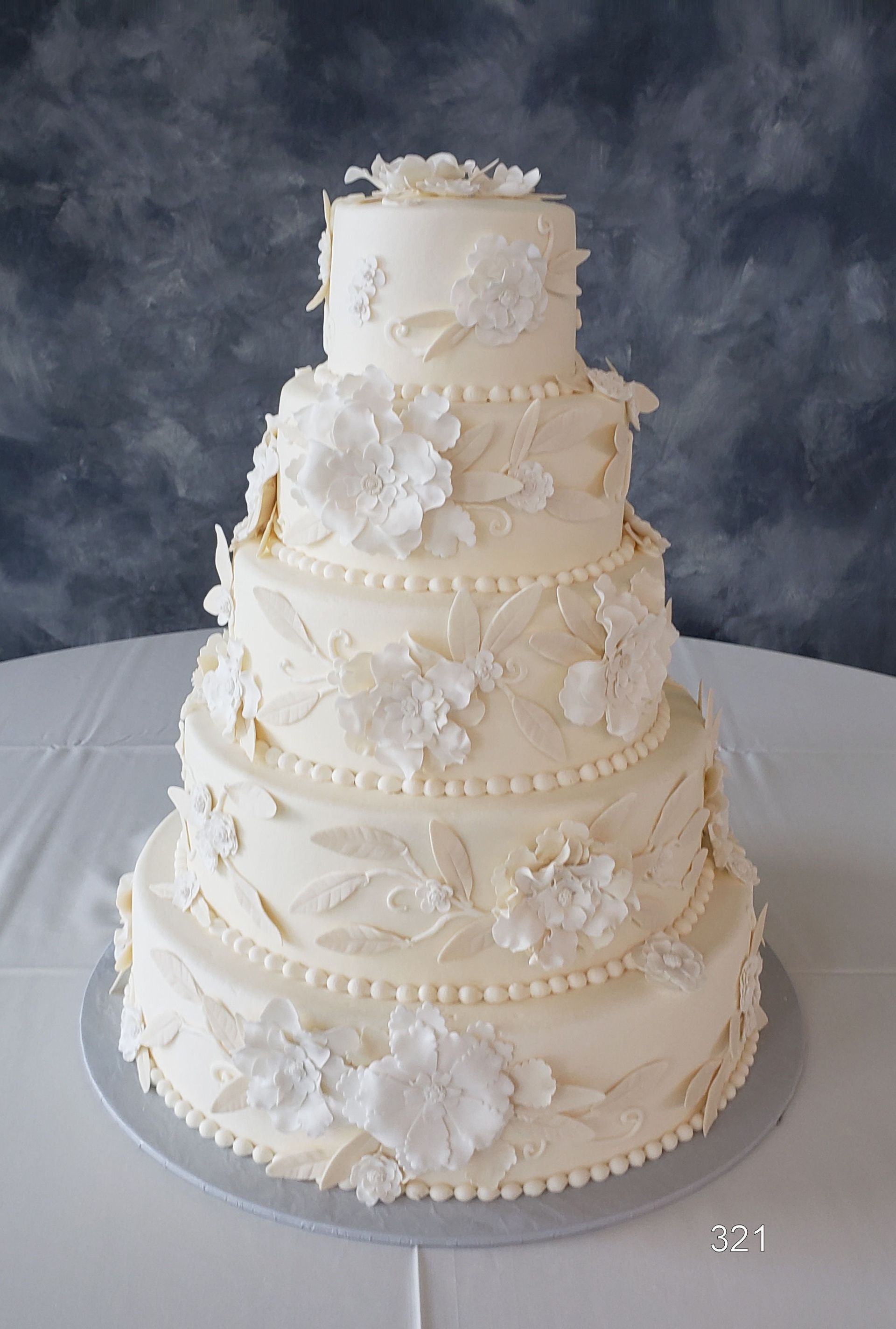 Four-tier white wedding cake with delicate floral decorations on a table against a dark backdrop