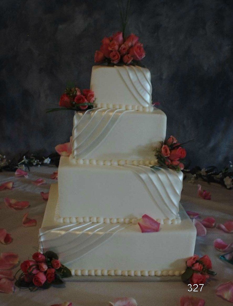 Four-tier white wedding cake with red rose decorations and petals on a dark backdrop