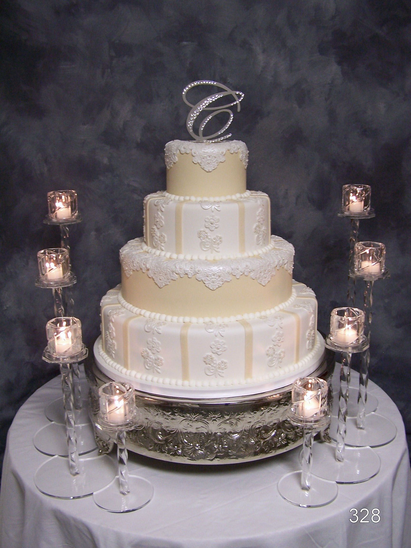 Tiered white wedding cake with pearl-like decorations, on a silver stand surrounded by glowing candles.