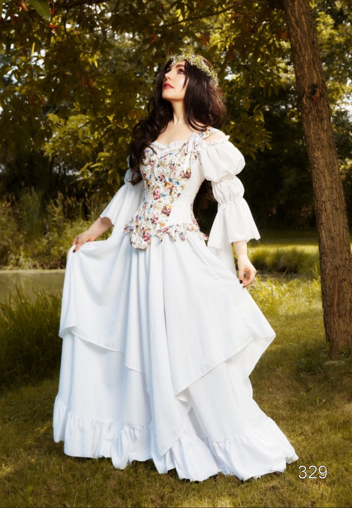 Person in a white floral dress standing in a wooded park, holding the skirt out.