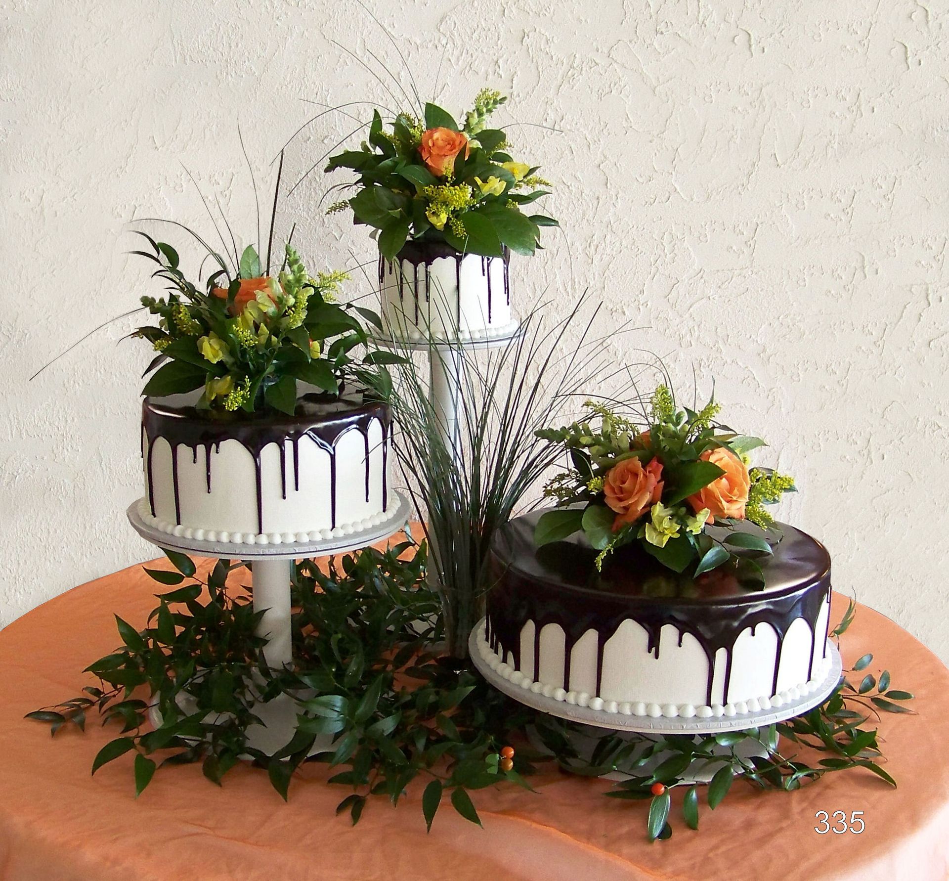 Three-tier chocolate drip cakes with orange flowers and green leaves on a wooden table