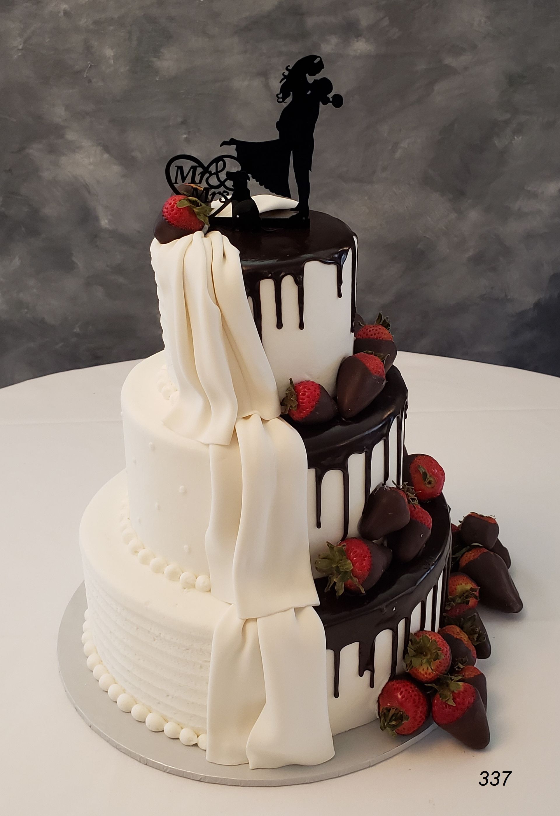 Three-tier white wedding cake with dark chocolate drip, red roses, and a black silhouette topper