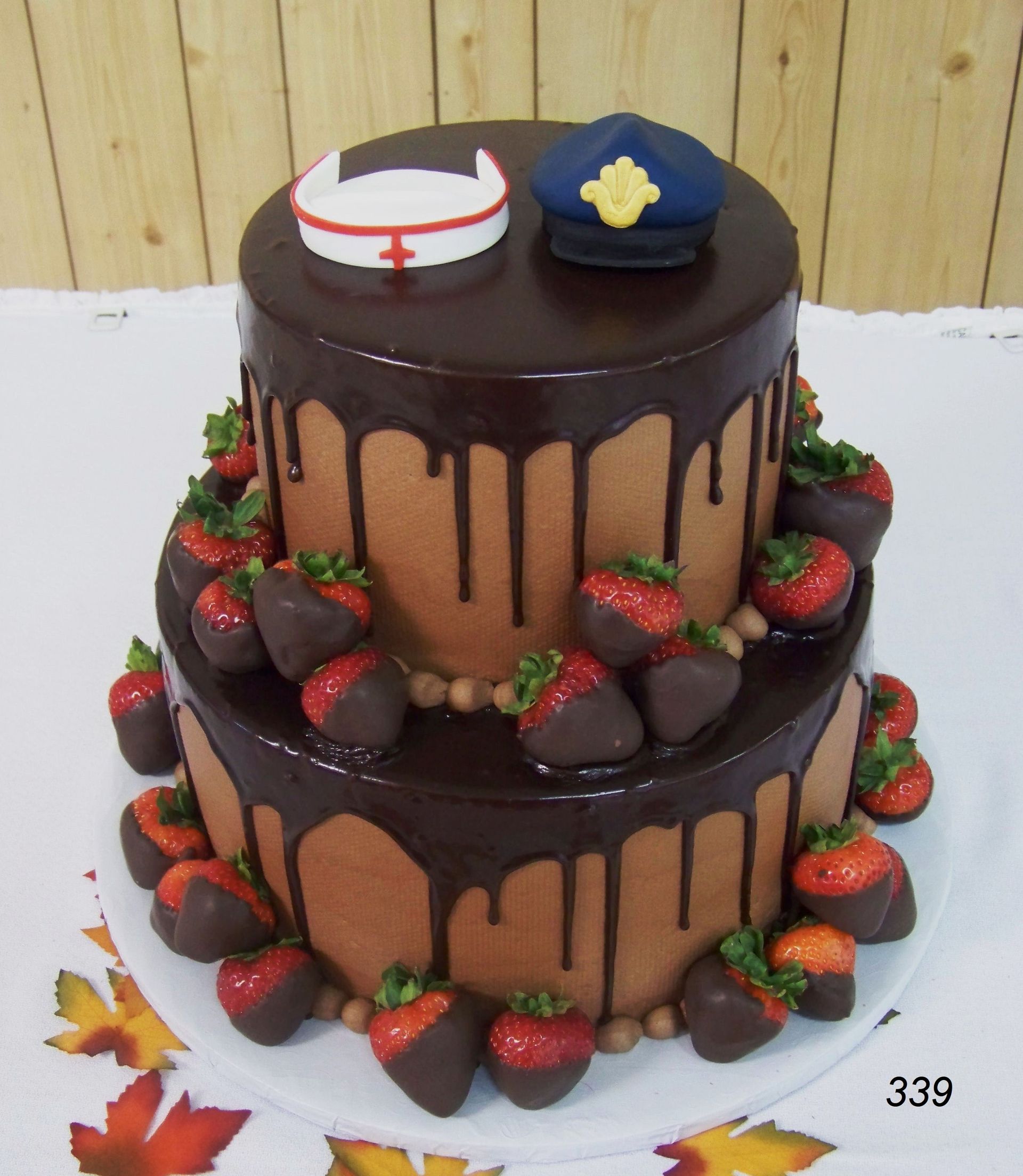 Two-tier chocolate drip cake topped with hats, decorated with strawberries and autumn leaves