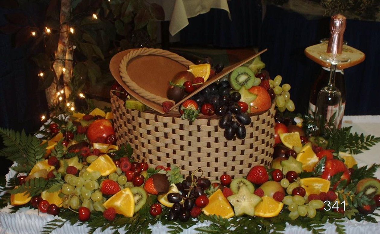 Decorative fruit basket centerpiece with grapes, apples, and pears on a table with candles