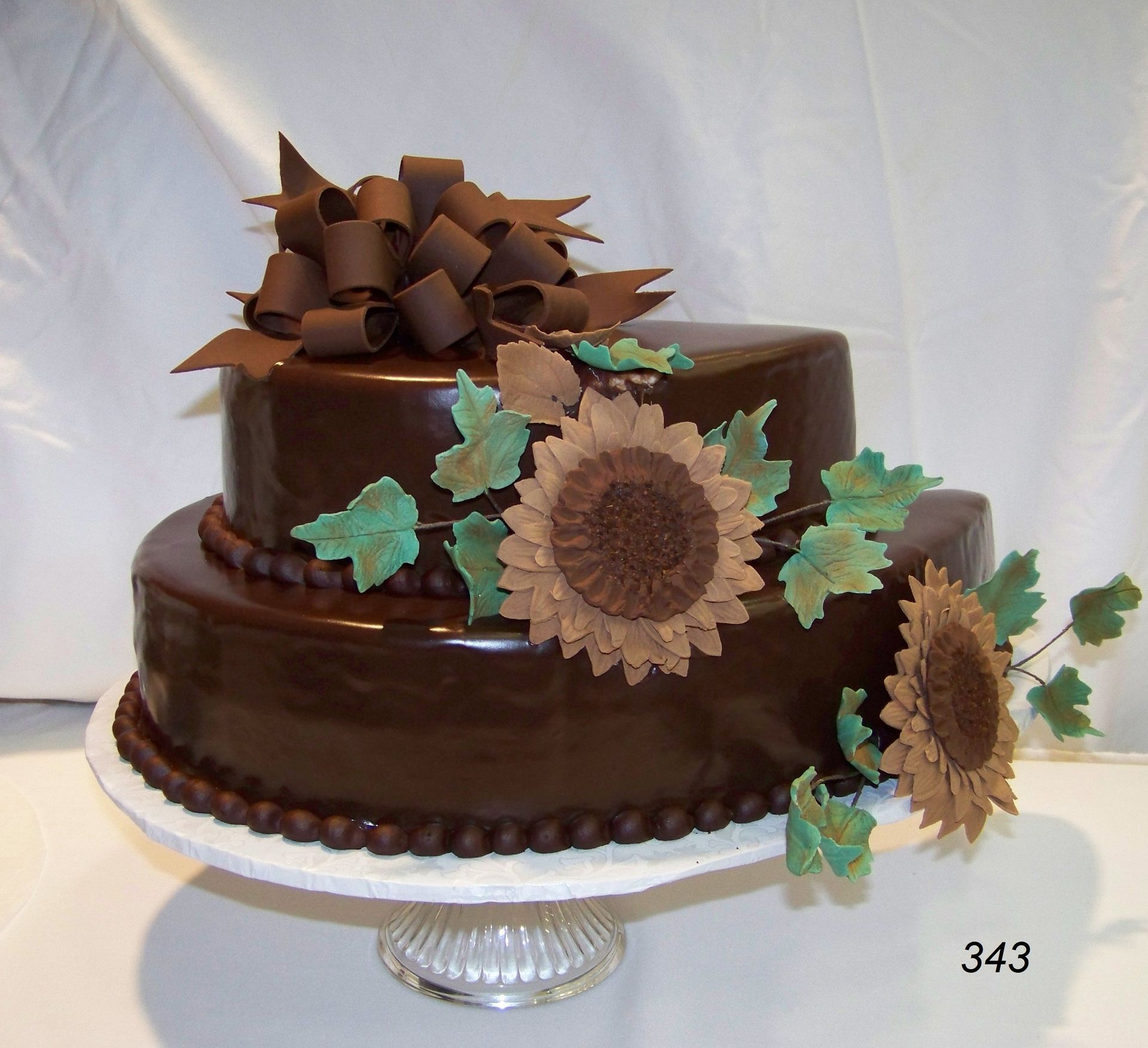 Chocolate cake with chocolate bow, sunflower decorations, and green leaves on a glass stand