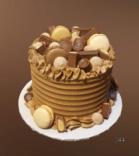 Tall chocolate-frosted cake topped with assorted cookies, macarons, and chocolates on a white plate