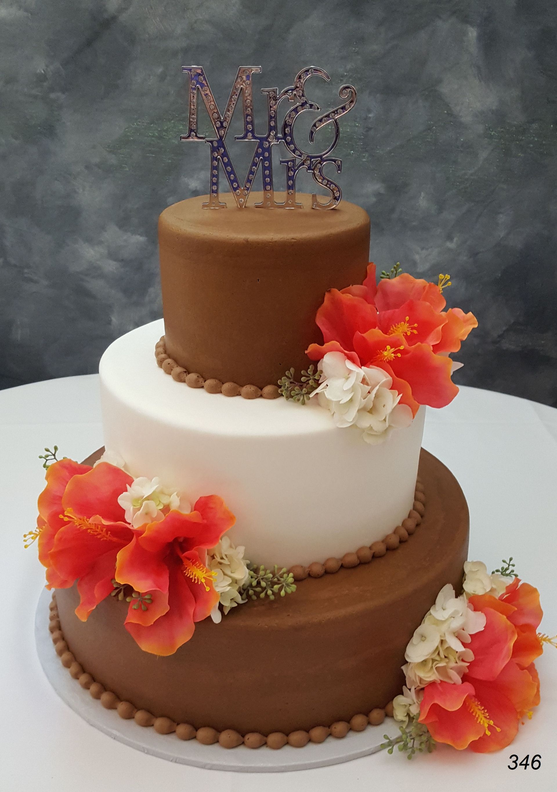 Three-tier wedding cake with brown and white layers, decorated with orange flowers and a monogram topper