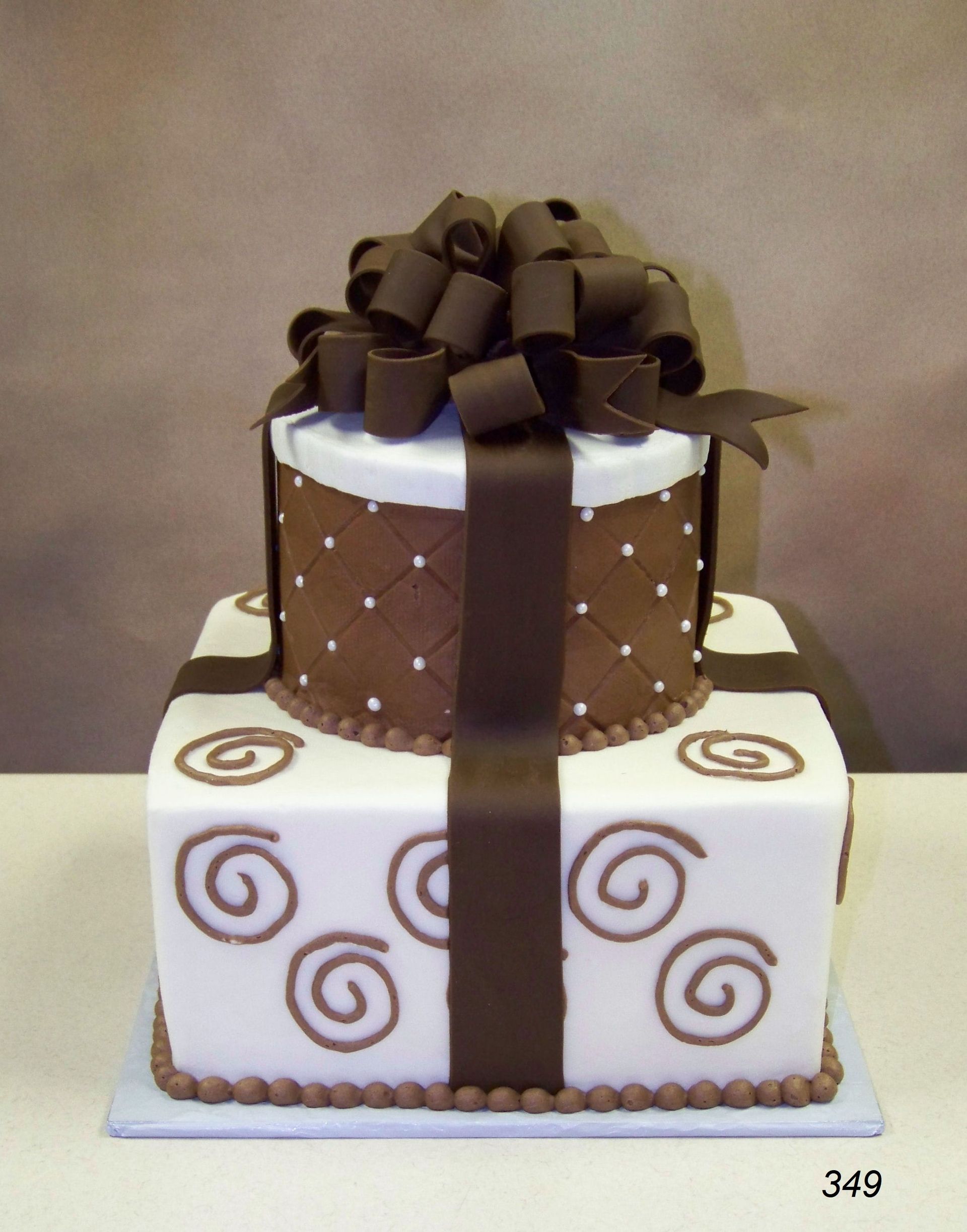 Two-tiered white and brown cake with spiral decorations and a large brown ribbon bow on top