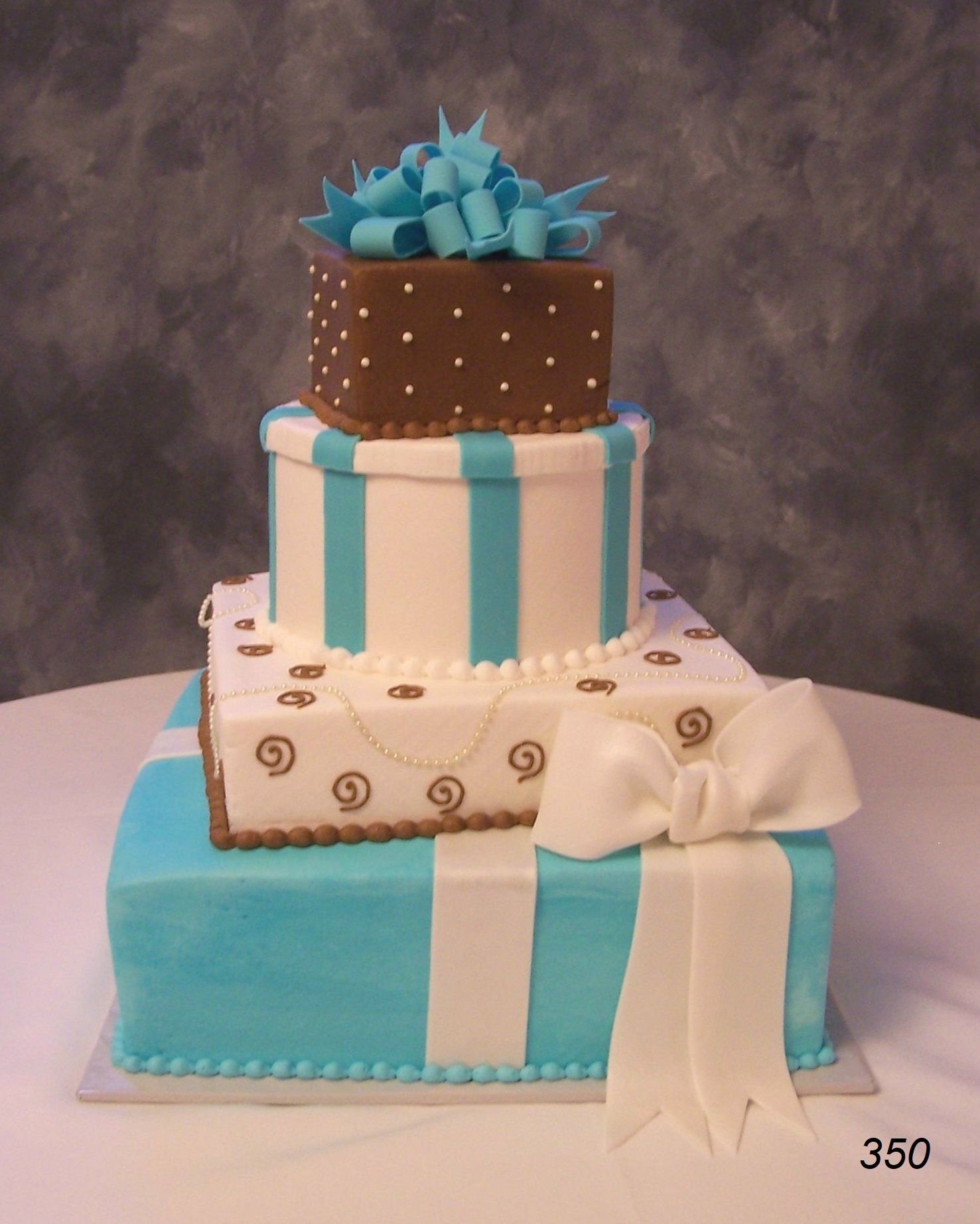 Three-tier decorated cake with turquoise, brown, and cream layers, topped with a blue bow and white ribbon accents
