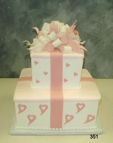 Two-tier gift box cake with pink ribbon and heart decorations, topped with a bow
