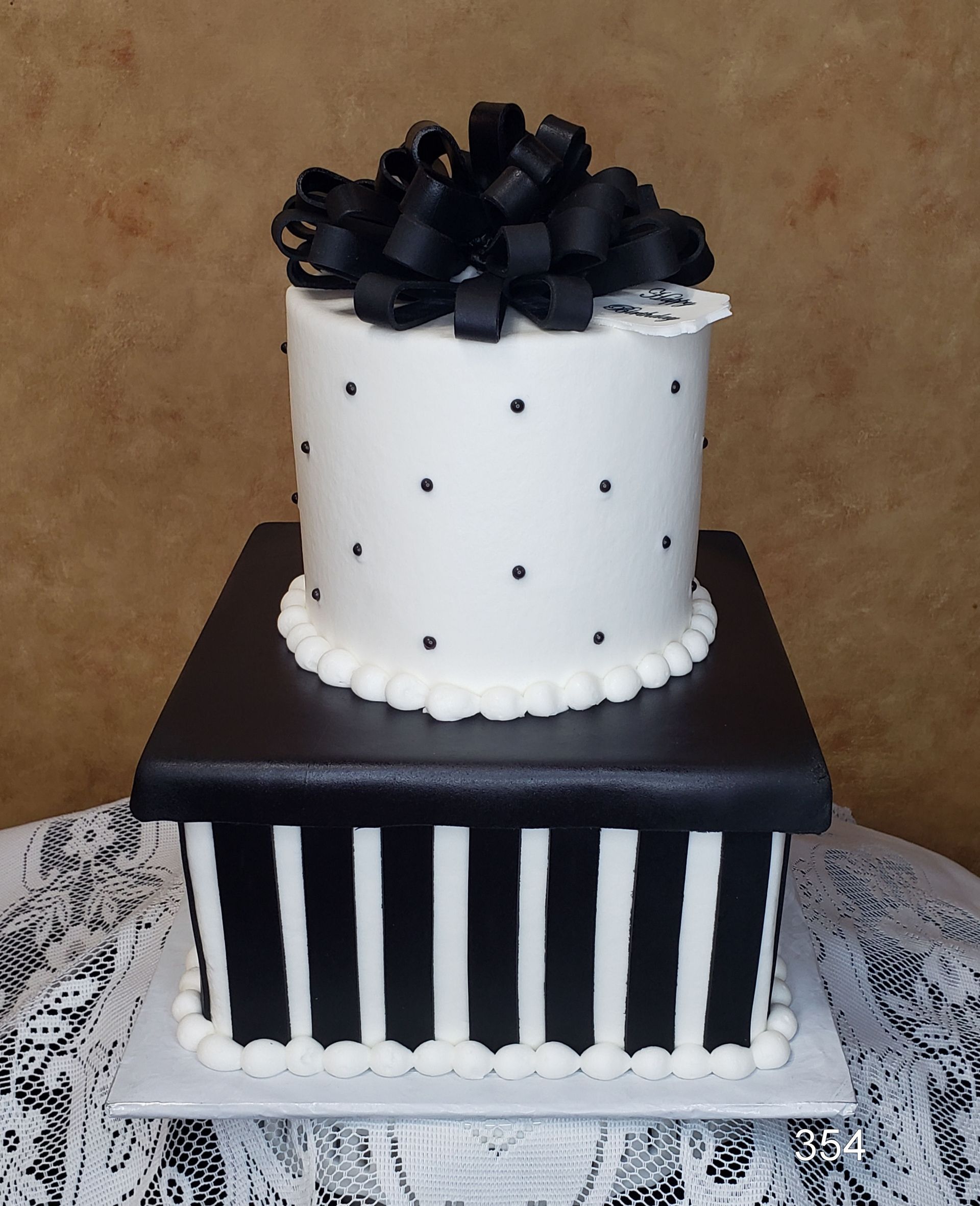 Black-and-white two-tier cake with striped lower tier and black bow on top on a lace-covered table
