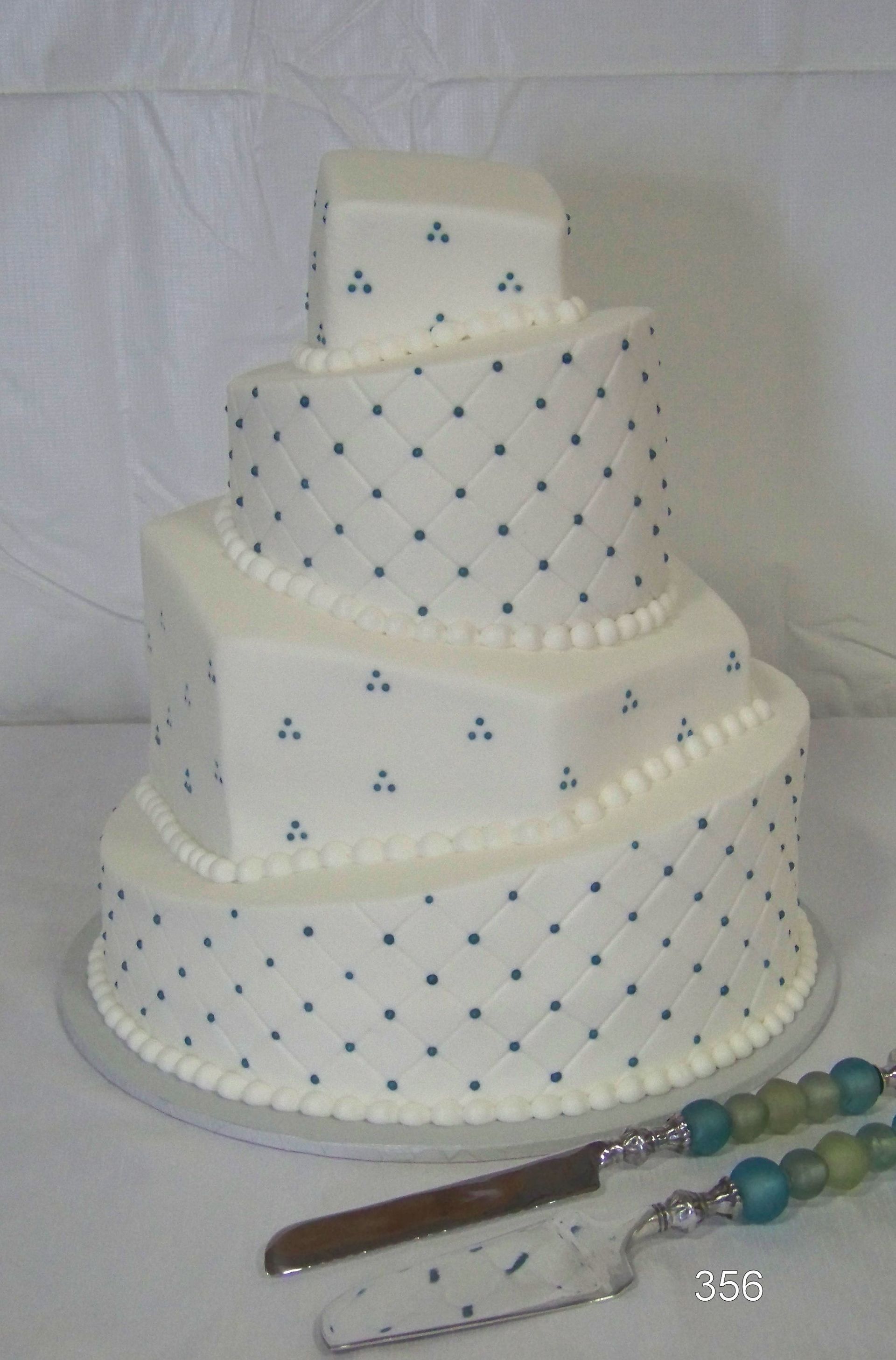 Three-tier white cake with blue dots and a silver cake server on a table