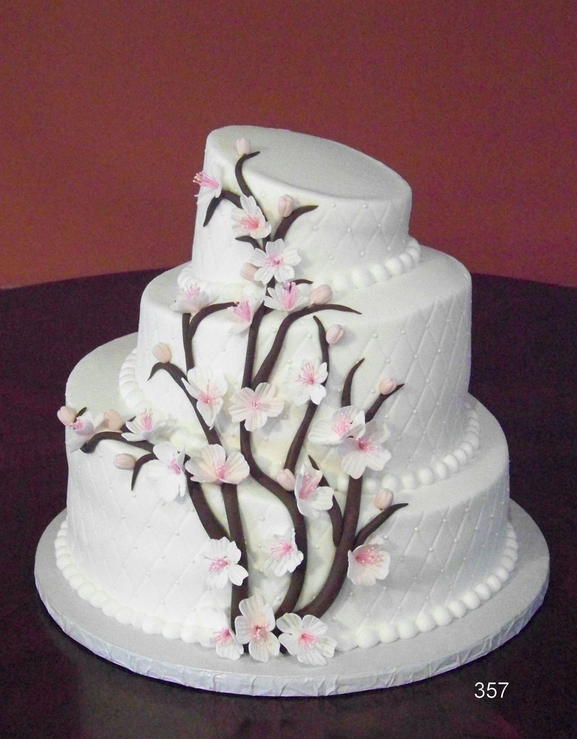 White tiered cake decorated with pink blossoms and dark branches on a burgundy background