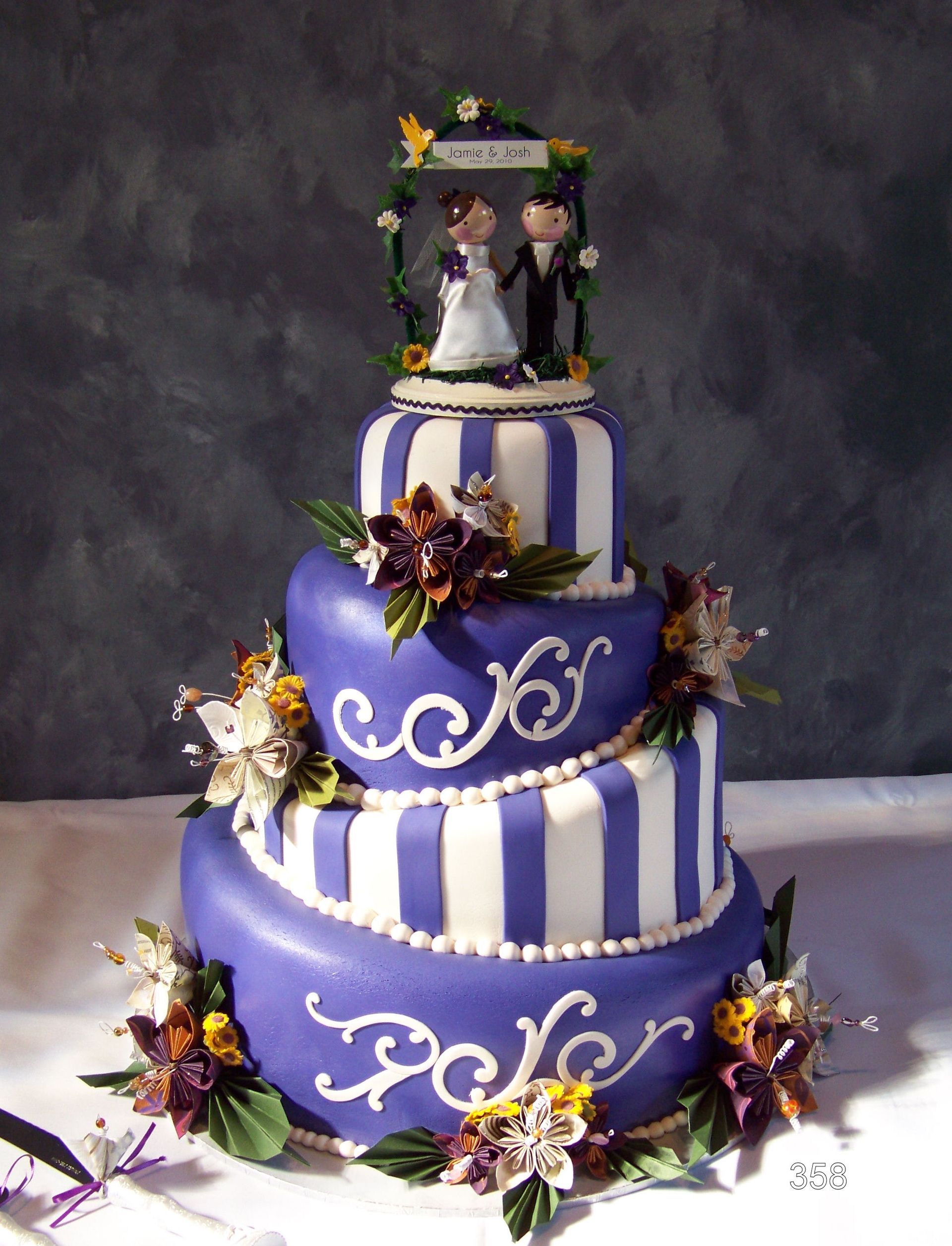 Purple and white tiered wedding cake with floral decorations and a bride-and-groom topper
