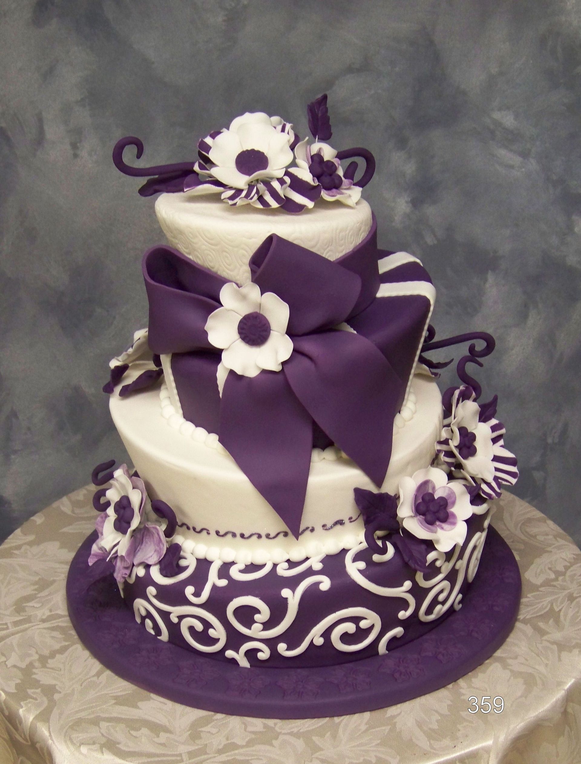 Three-tier white cake with purple ribbon bows and floral decorations on a purple cake board