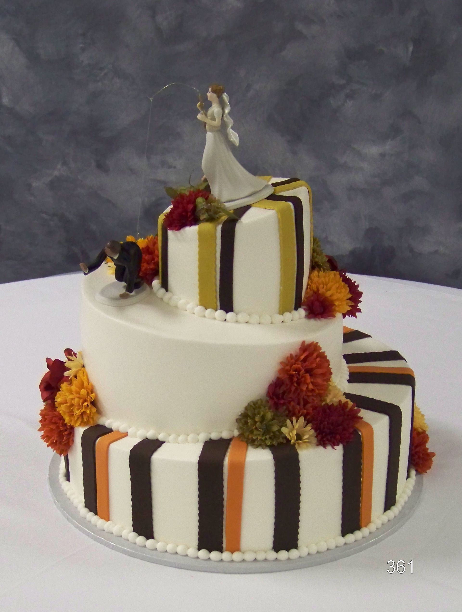 Three-tier white cake with black, gold, and orange stripes, topped with a figurine and marigold flowers