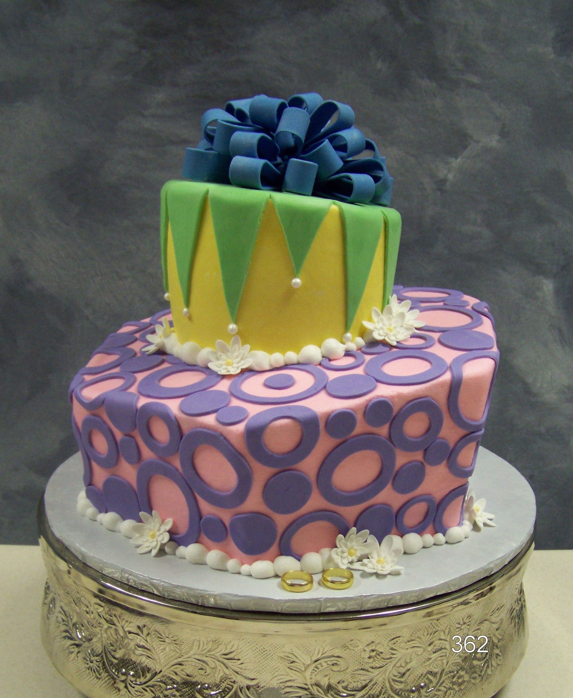 Decorated two-tier cake with purple and pink patterns, green accents, and a blue bow on top
