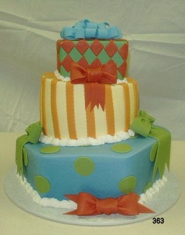 Three-tier decorated cake with blue, white, and orange tiers, bows, and polka dots on a white cloth background