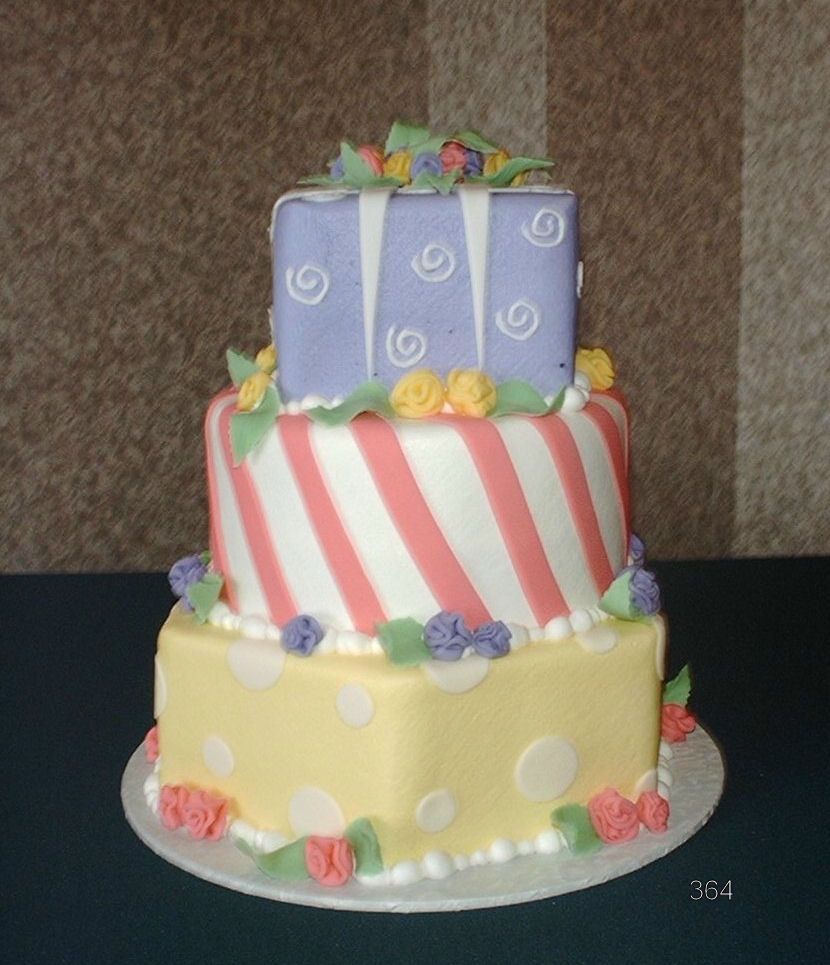 Three-tier frosted cake with pastel decorations and striped middle tier on a white plate
