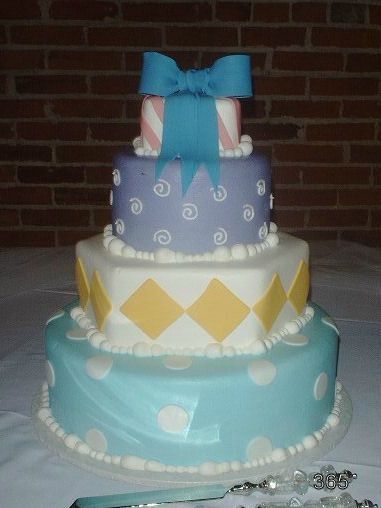 Three-tier decorated cake in blue, white, and yellow with a large blue bow topper