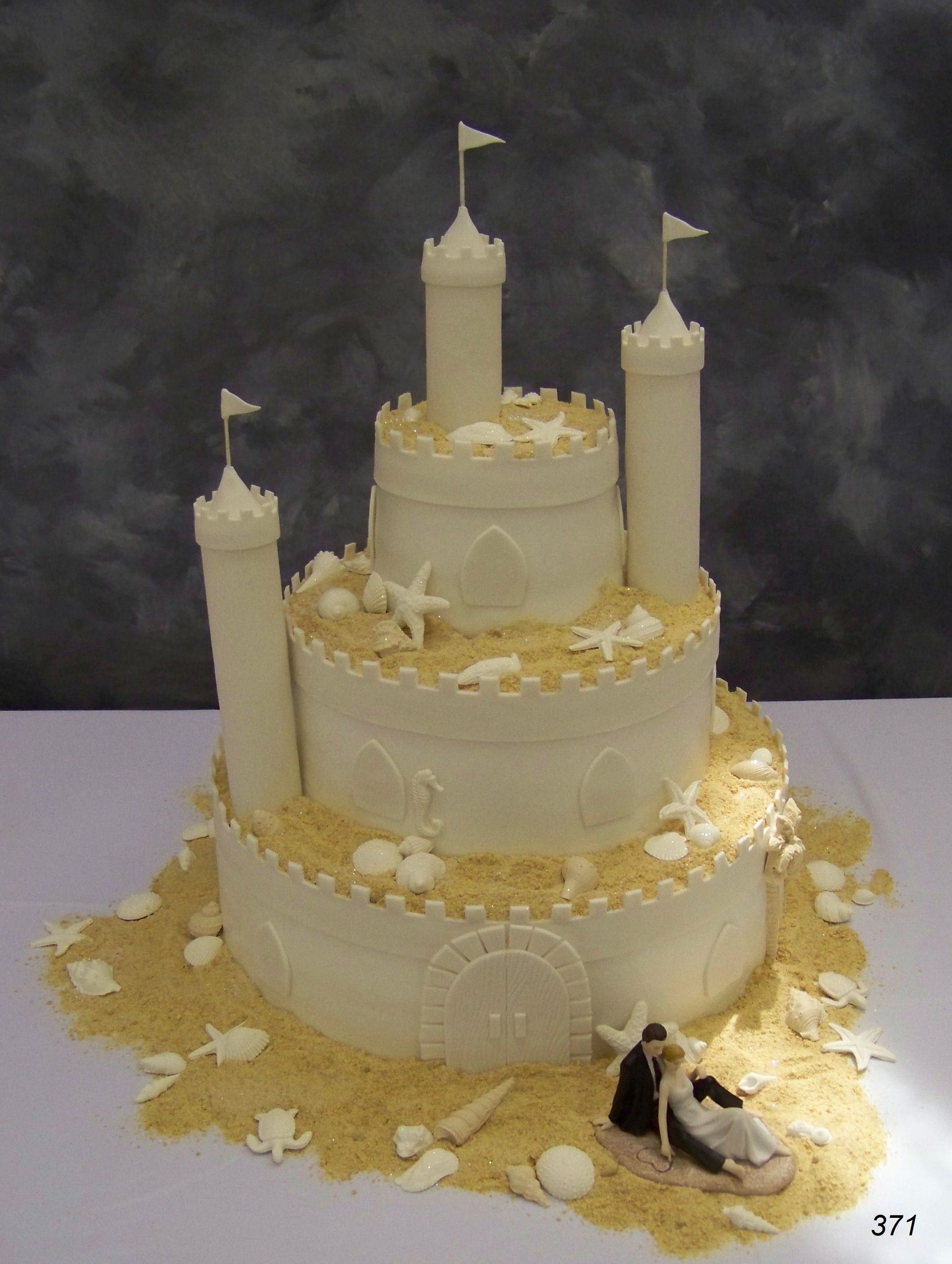 White tiered wedding cake with gold accents, small flags, and a miniature bride and groom figurine at the base
