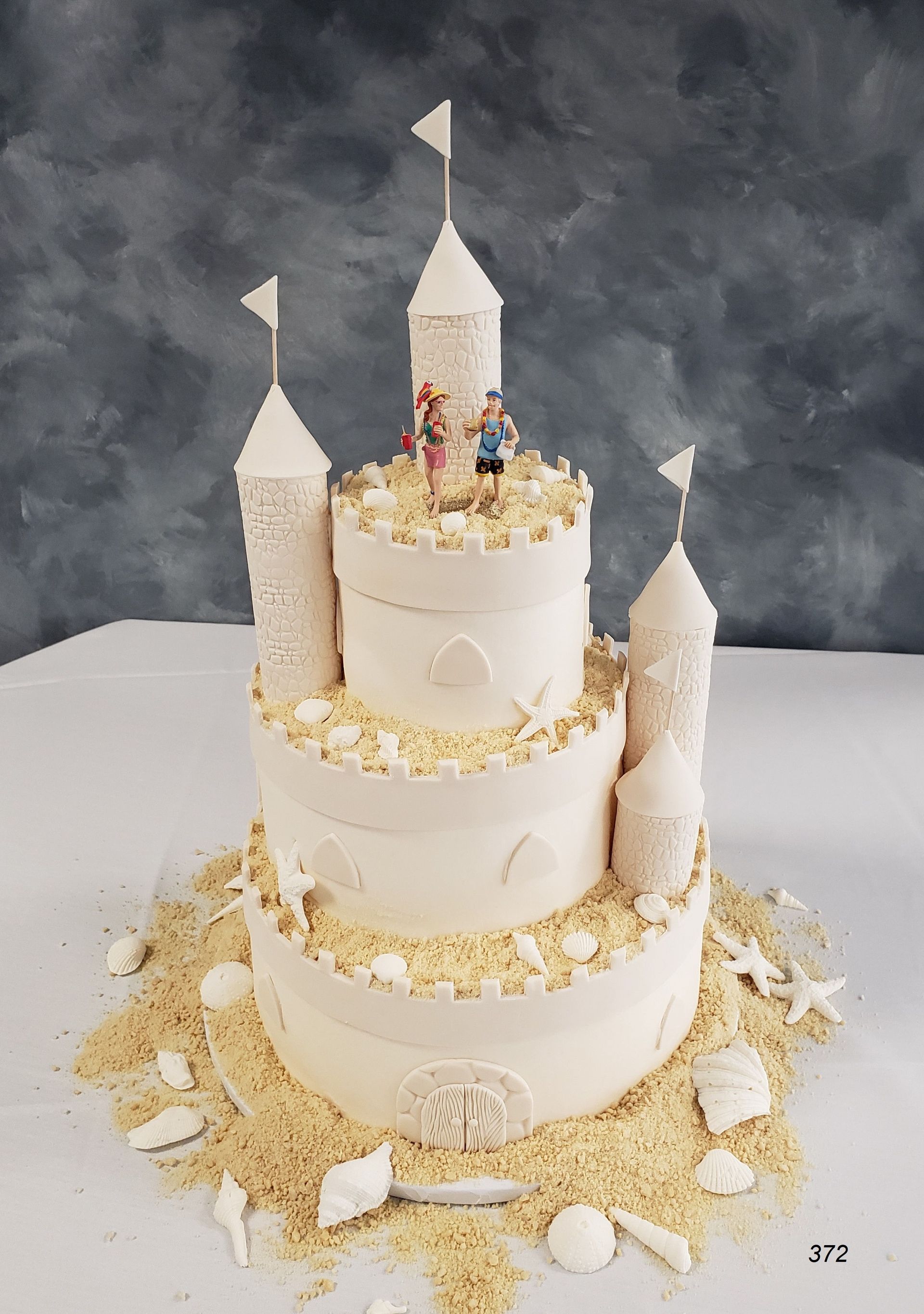 White castle-themed tiered cake with gold accents on a table, decorated with towers and flags
