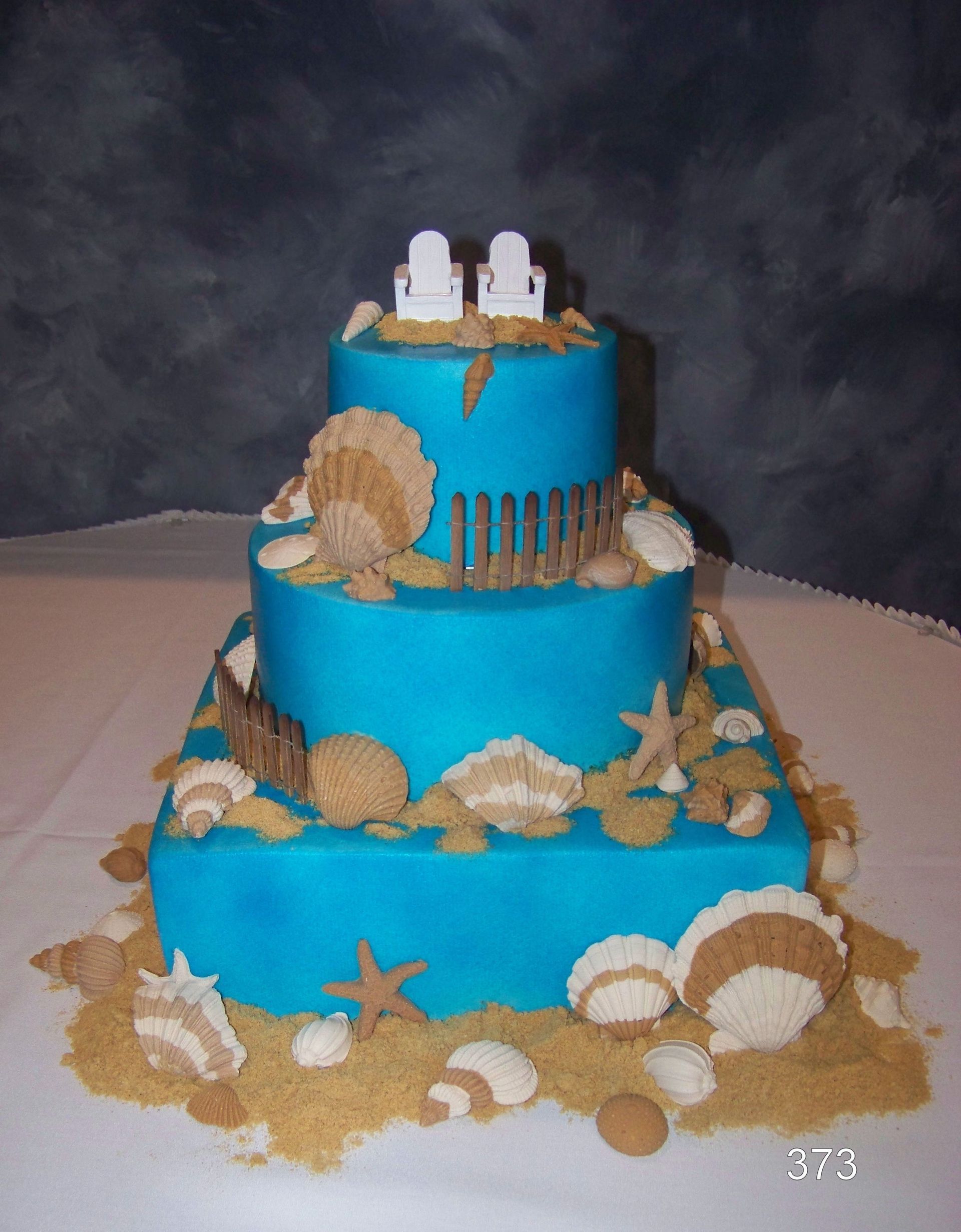 Three-tier blue cake with seashell decorations and white toppers on a table
