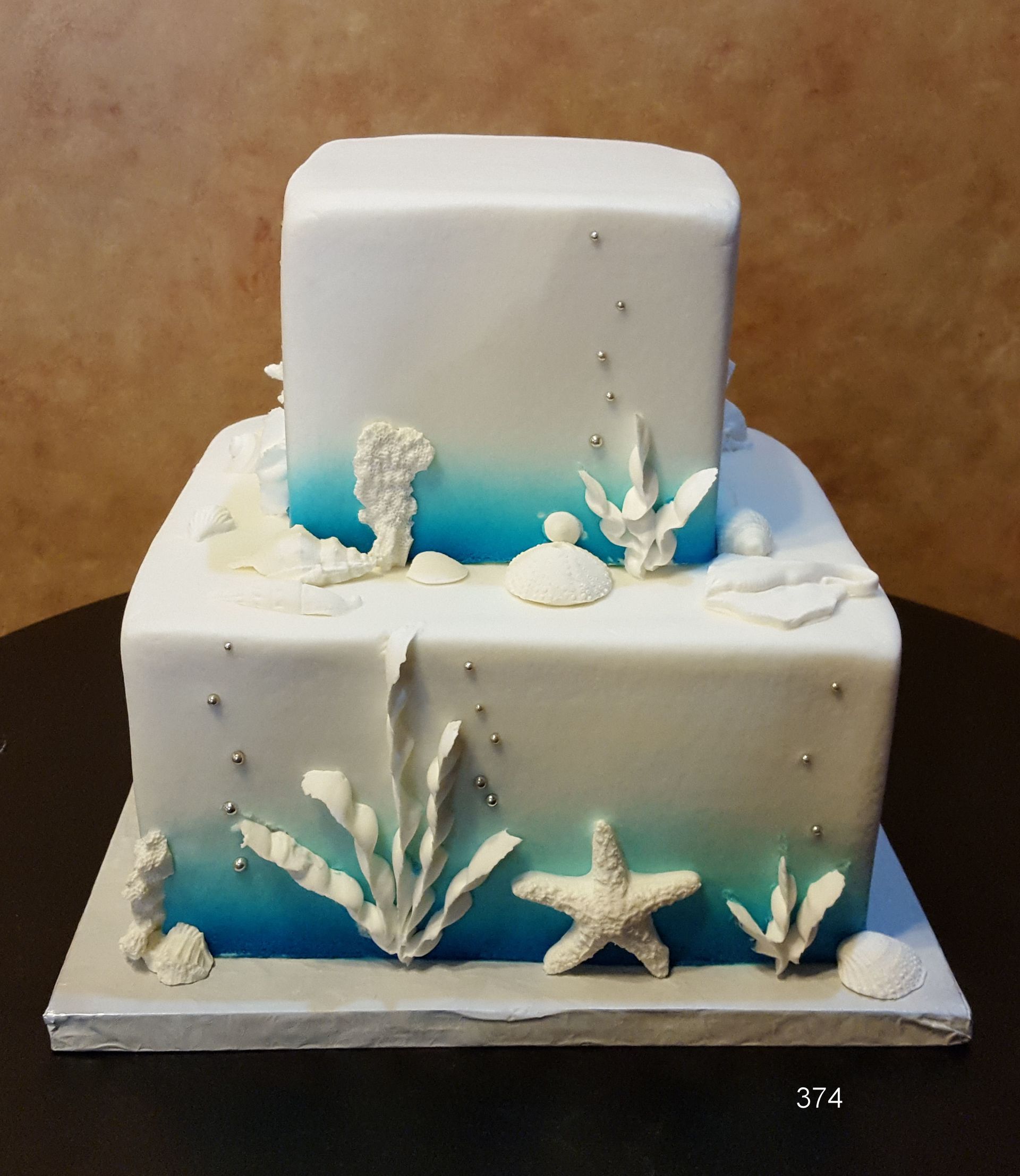 Two-tier white cake with blue accents and white sea-themed decorations on a board