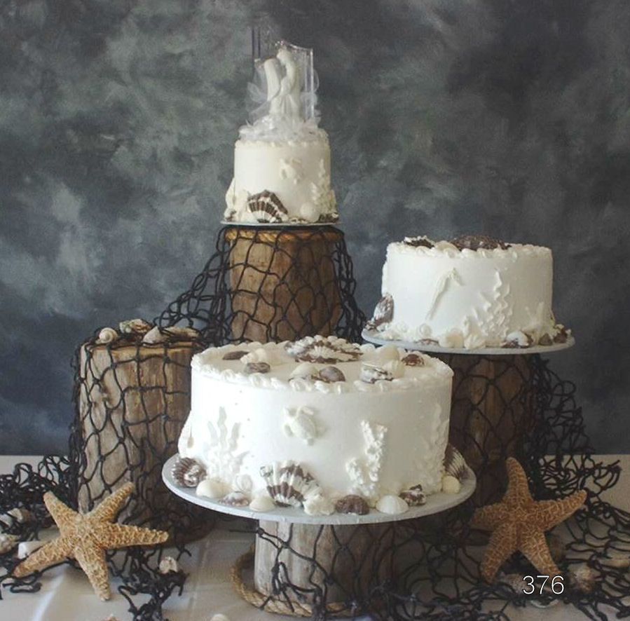 Three white frosted cakes on black wire stands with starfish decorations against a dark backdrop