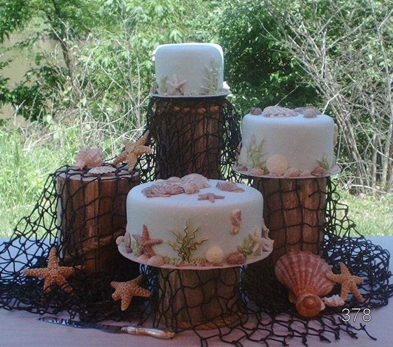 Three white decorated cakes on rustic wood stands with starfish and seashells outdoors