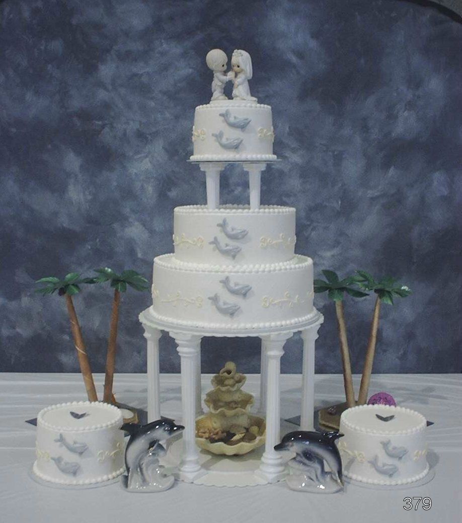 Decorative white tiered cake with dolphin and shell accents on a seaside-themed display table