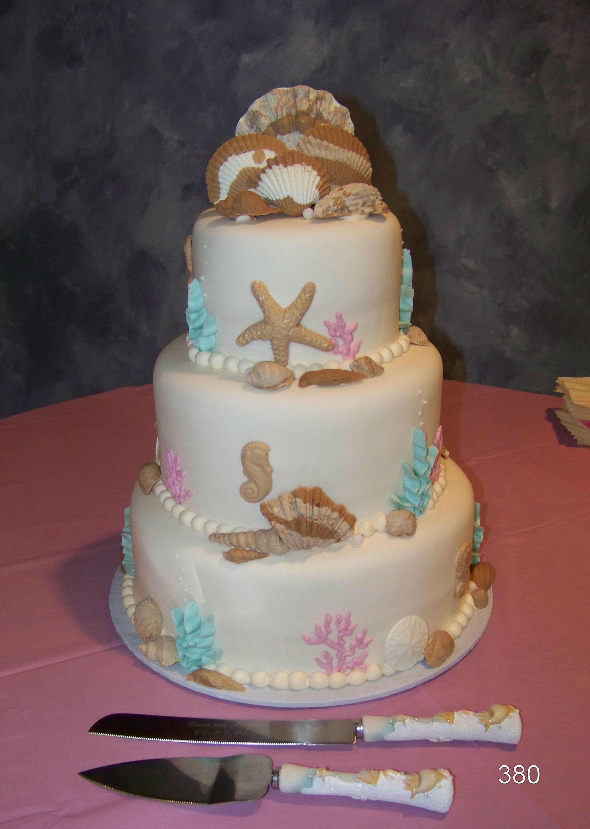 Three-tier white cake decorated with seashells and starfish on a pink tablecloth