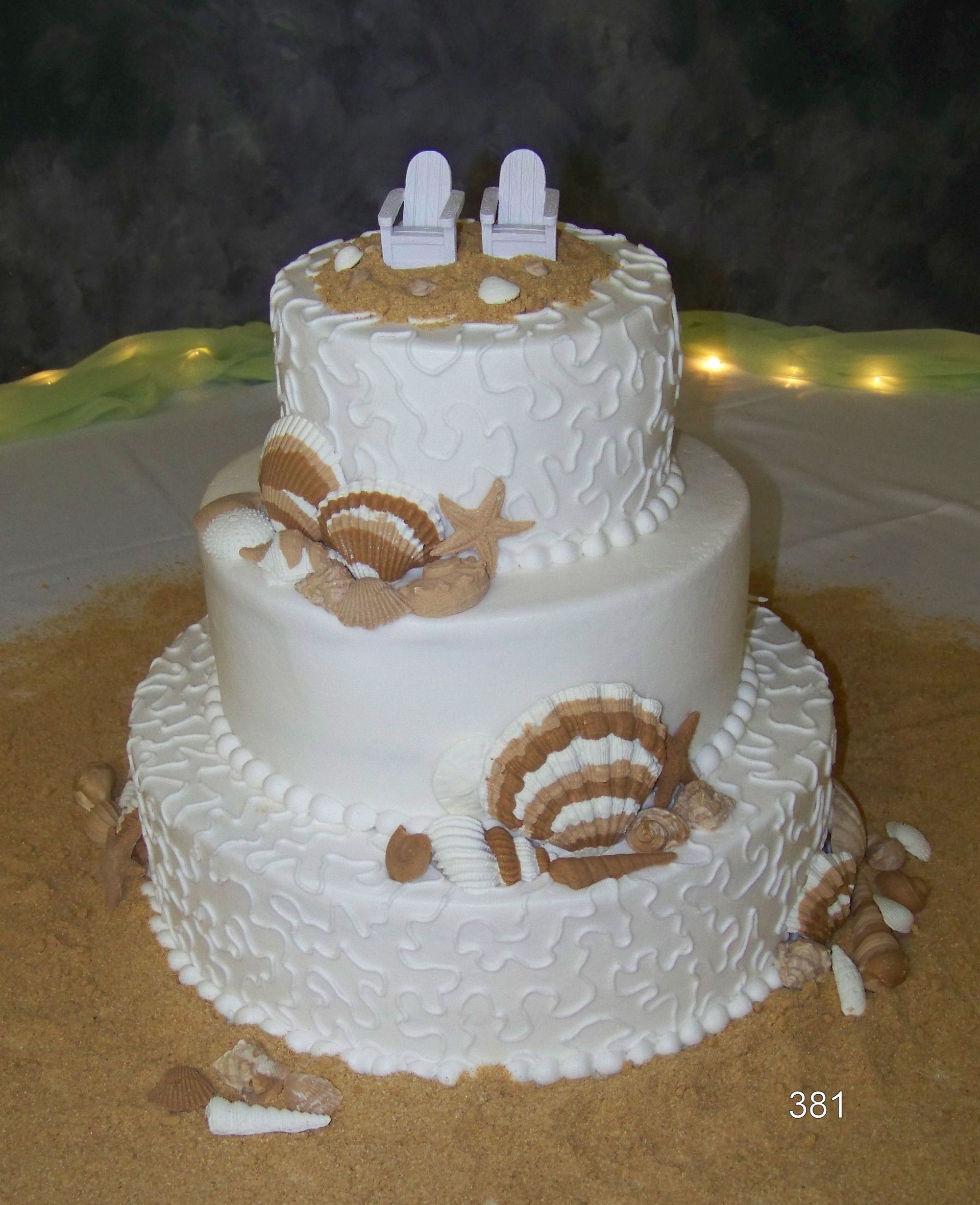 Three-tier white wedding cake with shell frosting and seashell decorations on a table.
