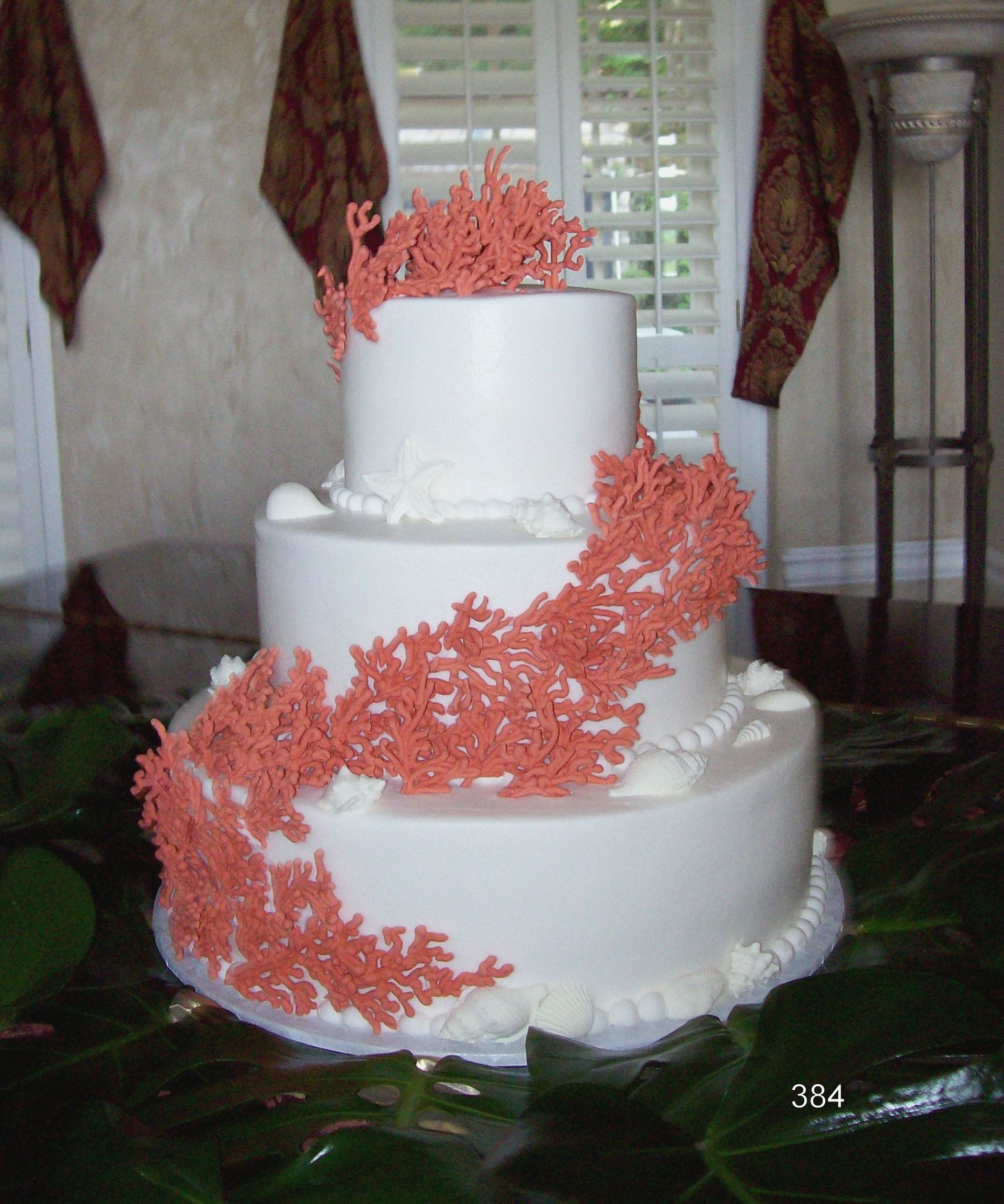 White three-tier cake with pink coral decorations on a table by a window