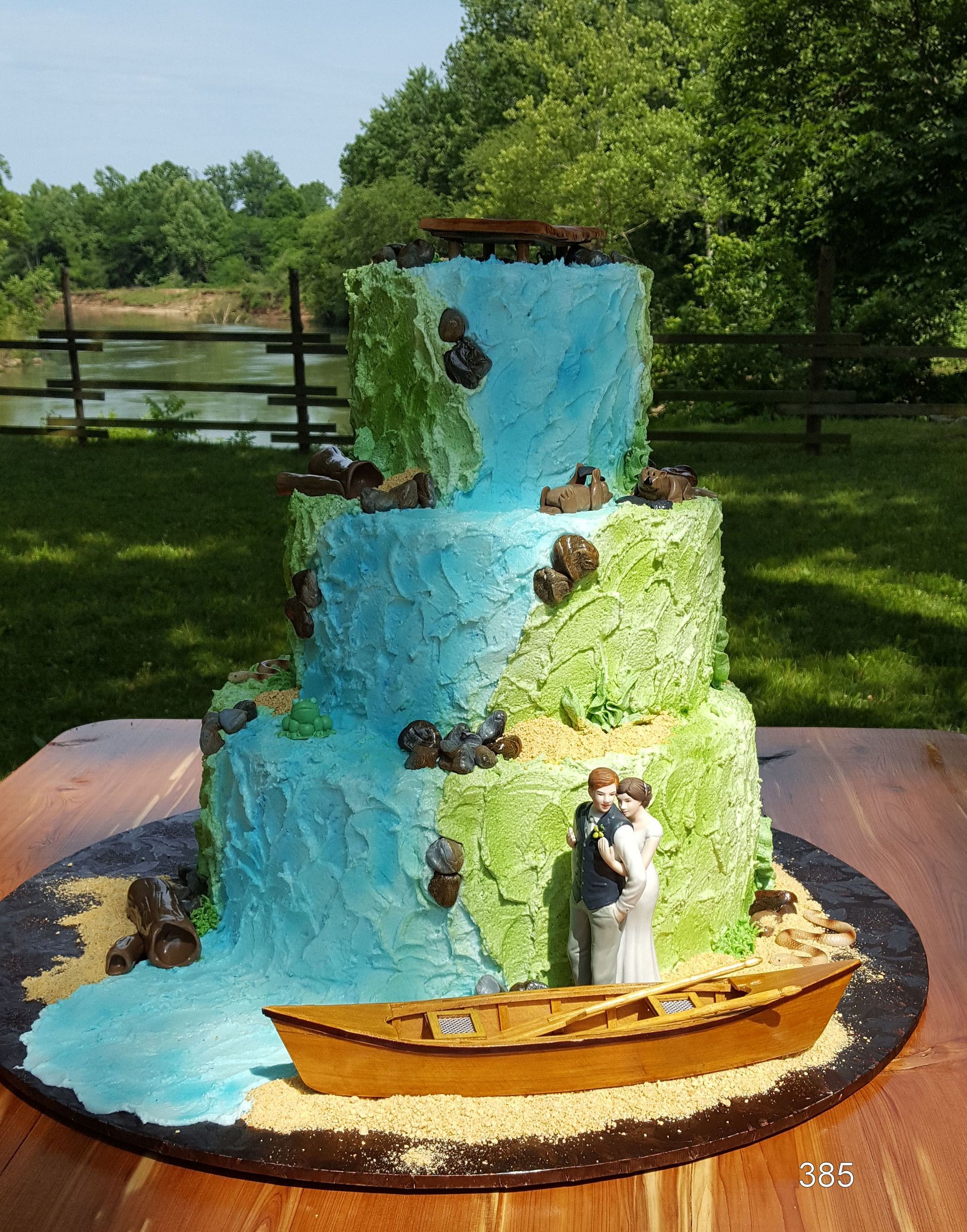 Small waterfall sculpture with blue water, rocks, and a canoe on a base in a grassy outdoor setting