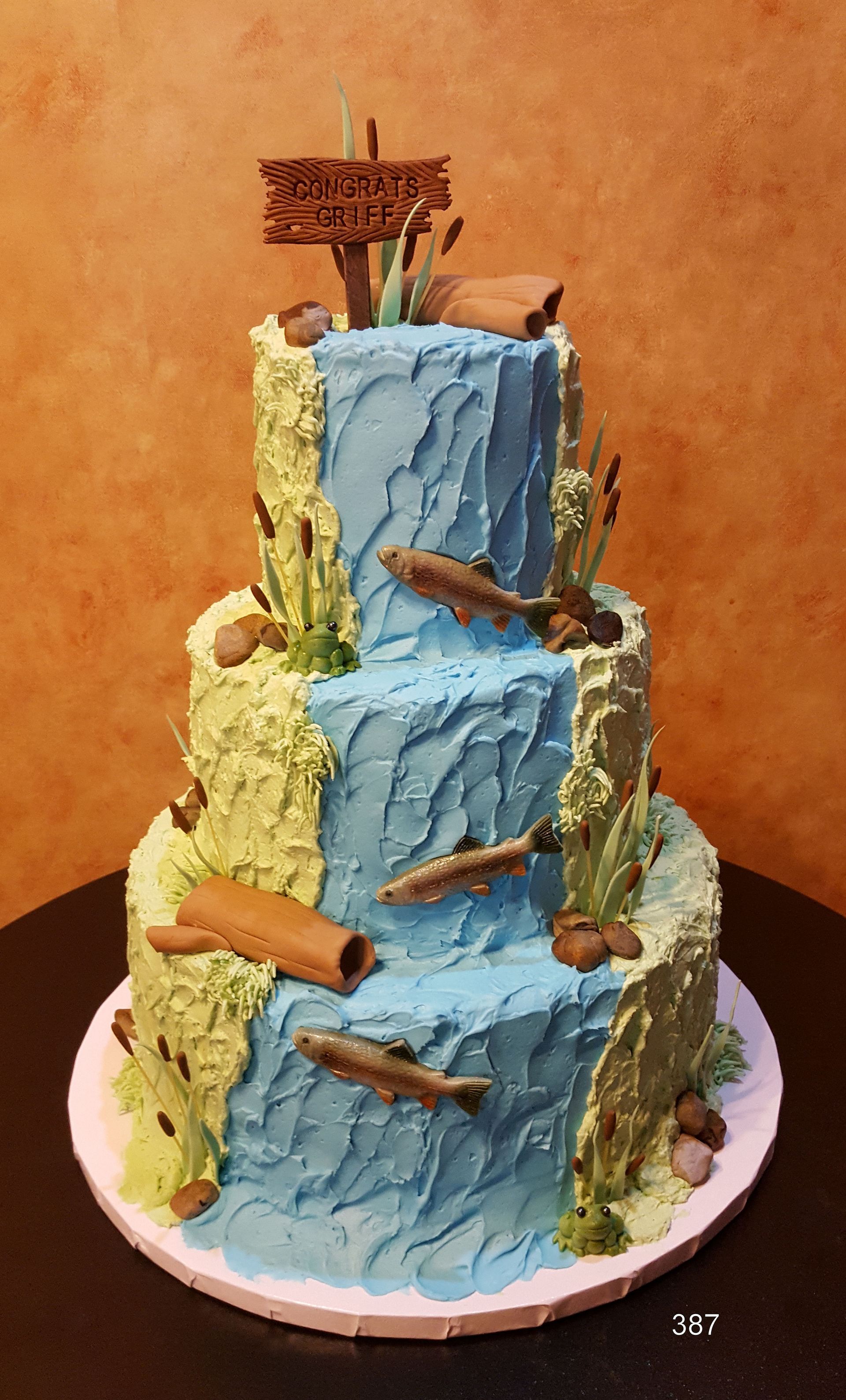 Three-tier blue and yellow cake with fish and a shipwreck-themed topper on a white plate