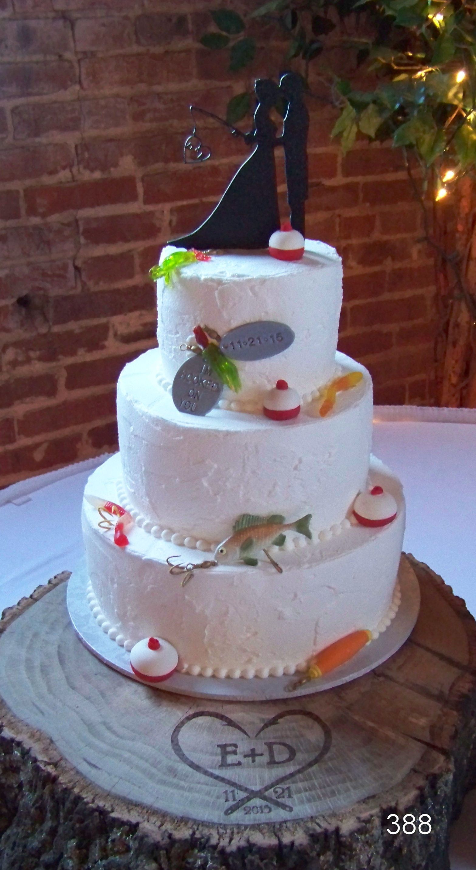 Three-tier white wedding cake with flowers and a black topper on a rustic wood stand