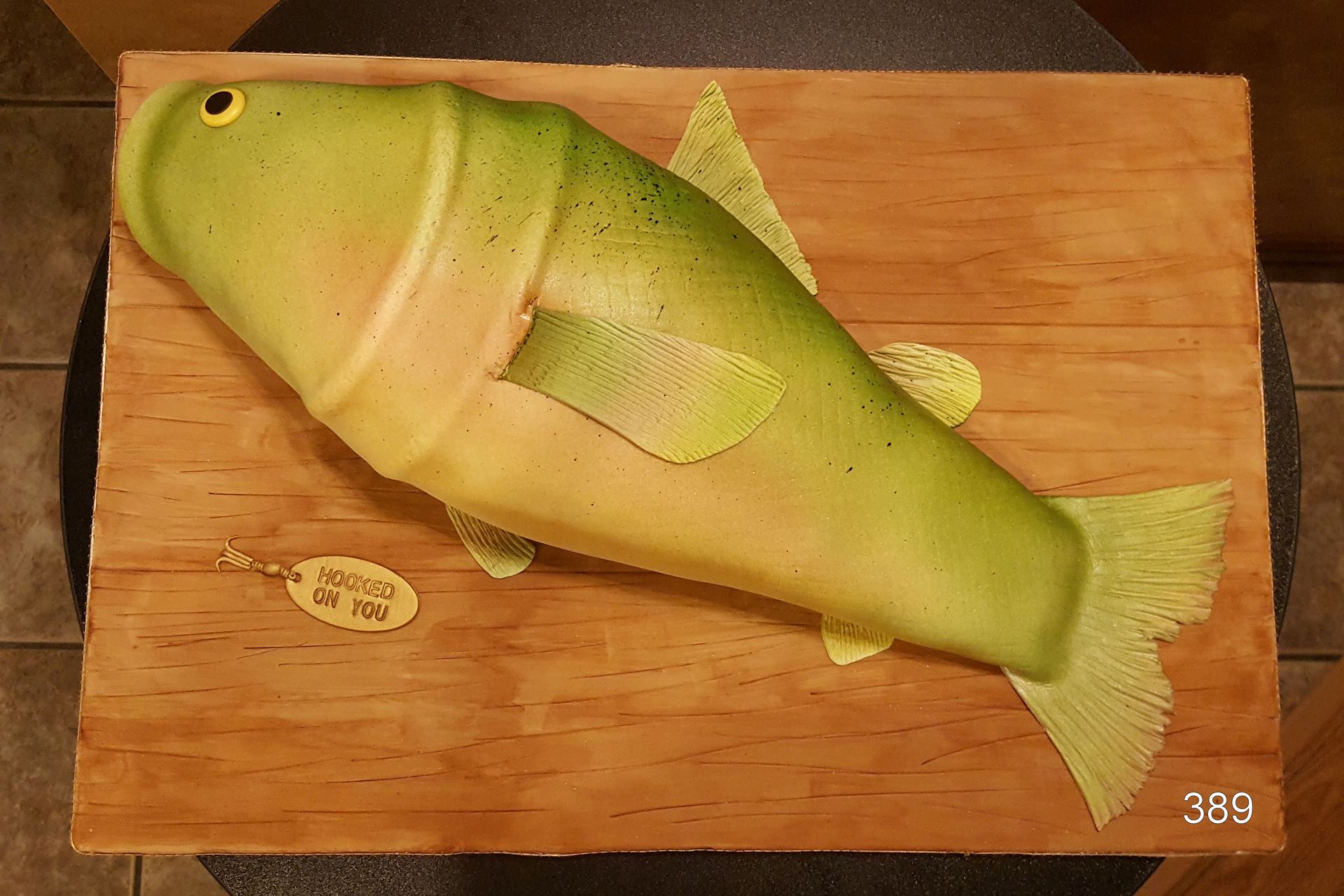 Green fish-shaped plush toy on a wooden board, with a small tag nearby.