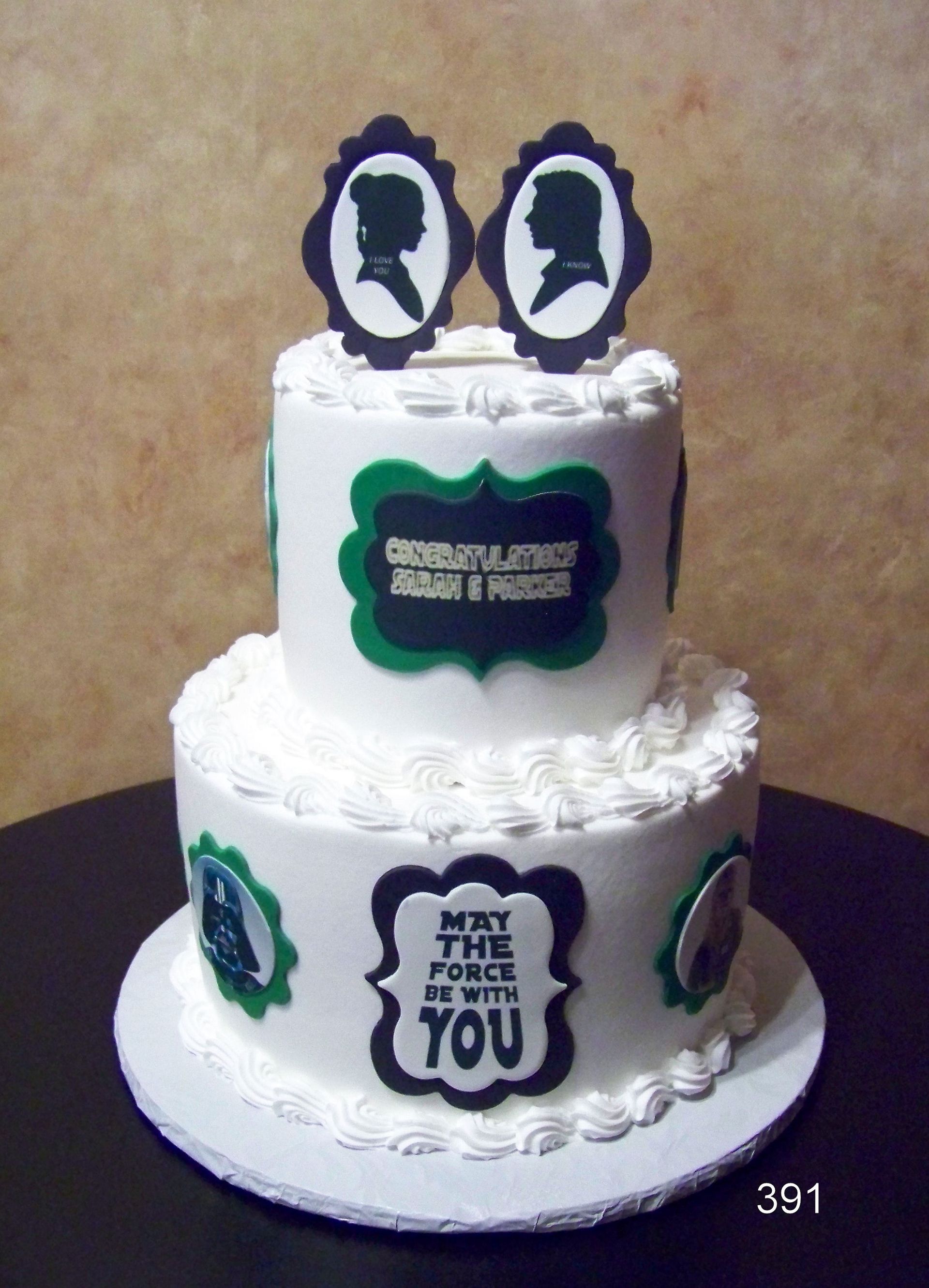 Two-tier white cake with green and purple plaques and two silhouette toppers, on a round cake board