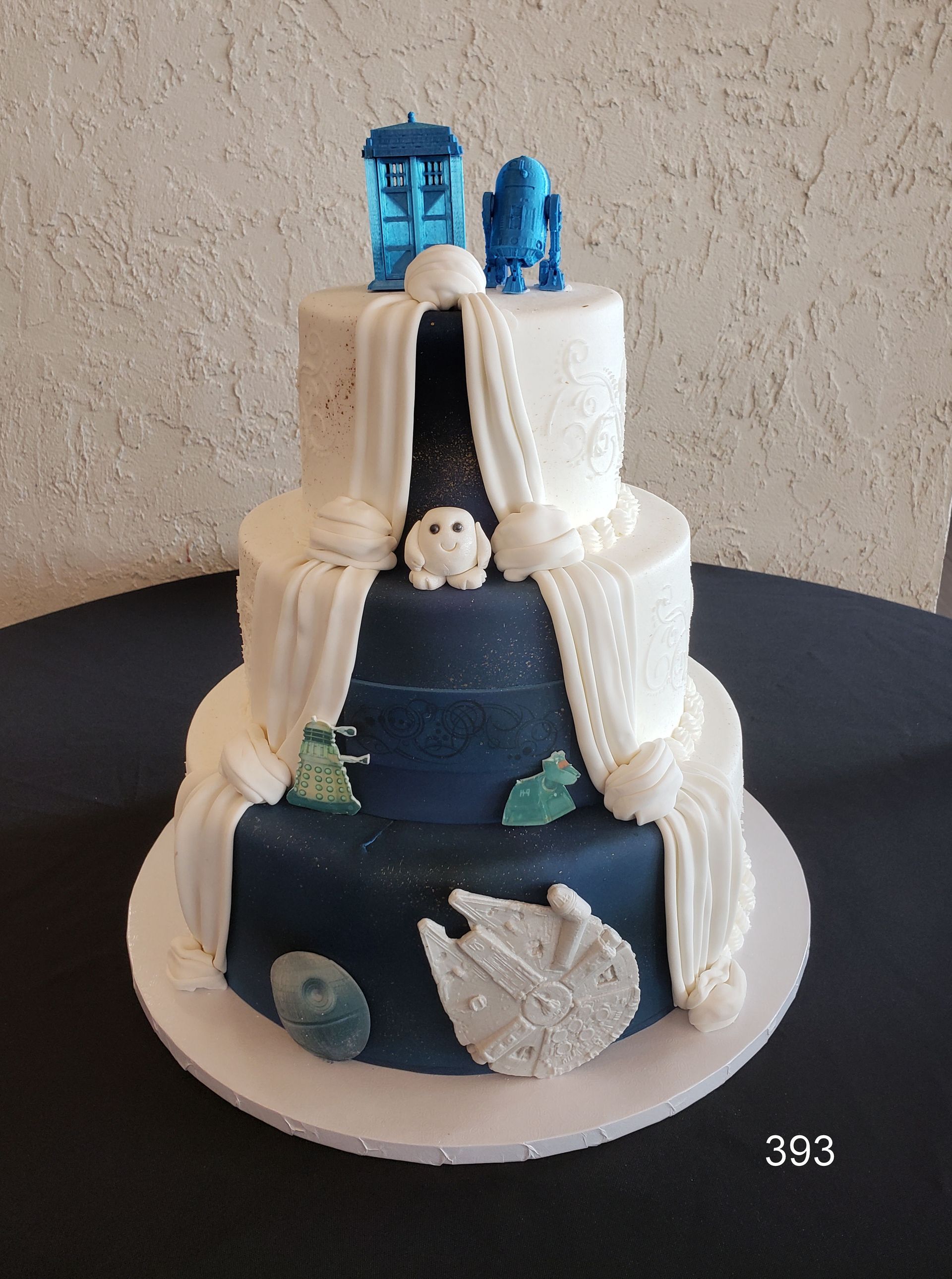 Blue and white tiered cake decorated with white drapes, shells, and small blue toppers on top