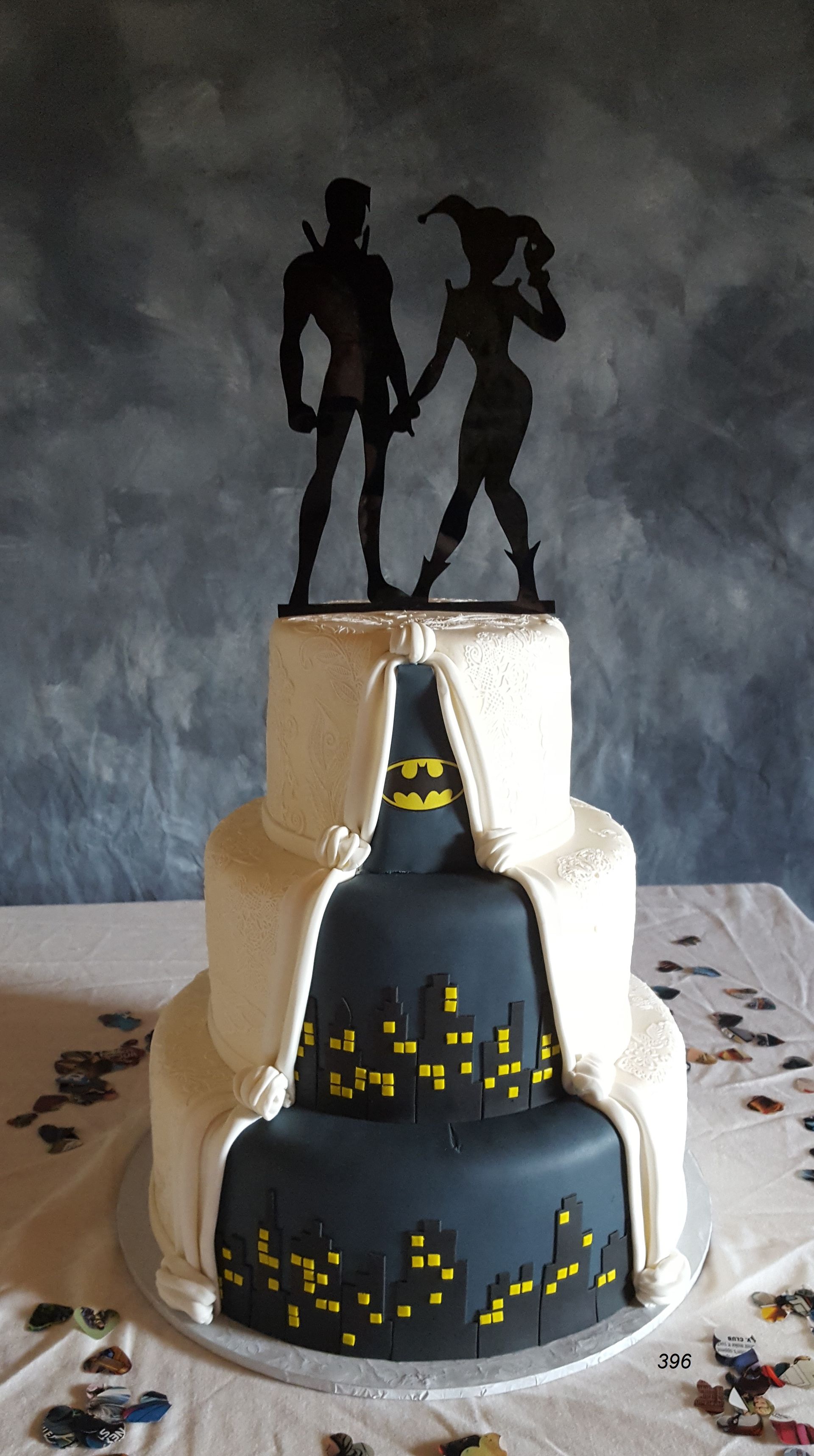 Black and gray tiered cake decorated like Gotham skyline with Batman and Catwoman silhouettes on top